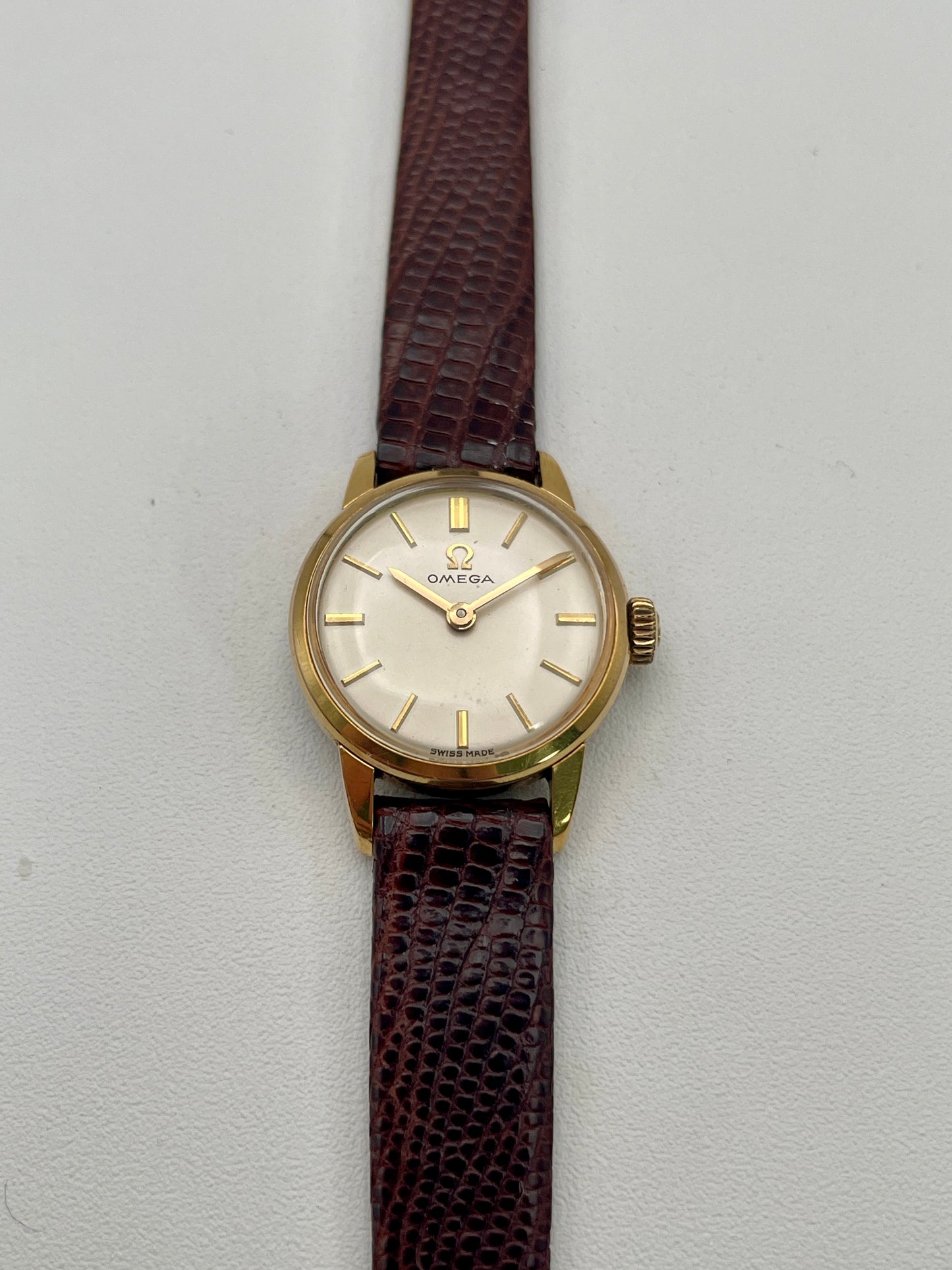 Front view of an Omega 511.015 Vintage Women's Watch in gold with a cream dial and gold baton indices, paired with a brown leather strap.
