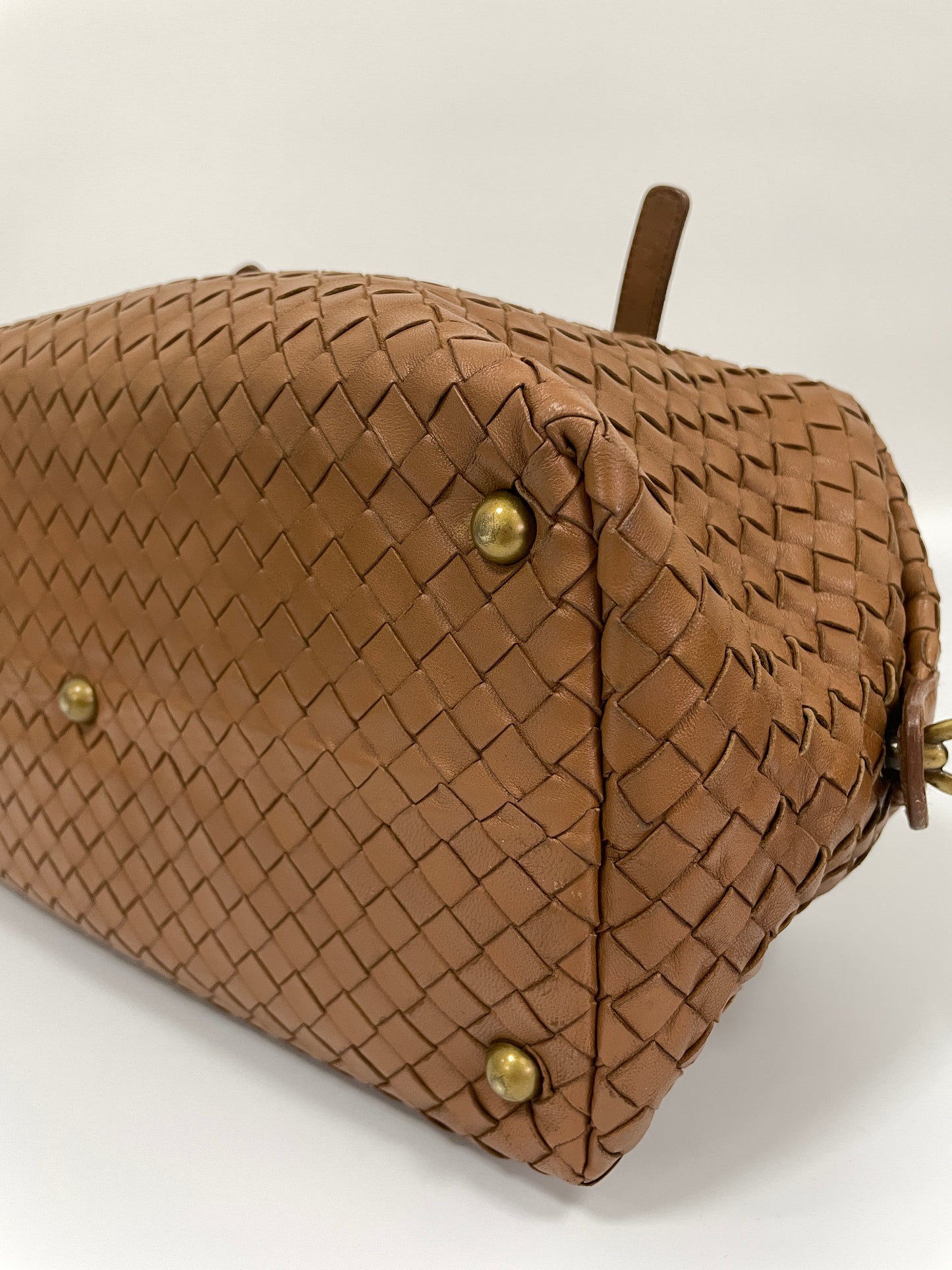 Close up bottom view of a Bottega Veneta Intrecciato Montaigne bag in brown leather showing the woven pattern and brass feet for protection.