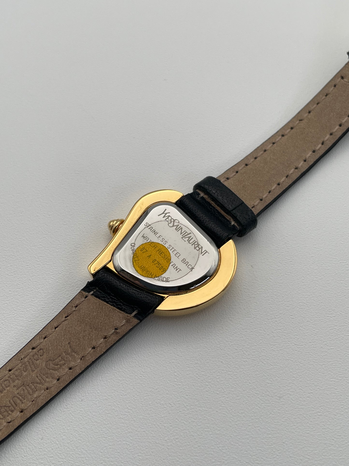 Back view of a YSL heart watch showing the stainless steel back with brand engraving and black leather strap.