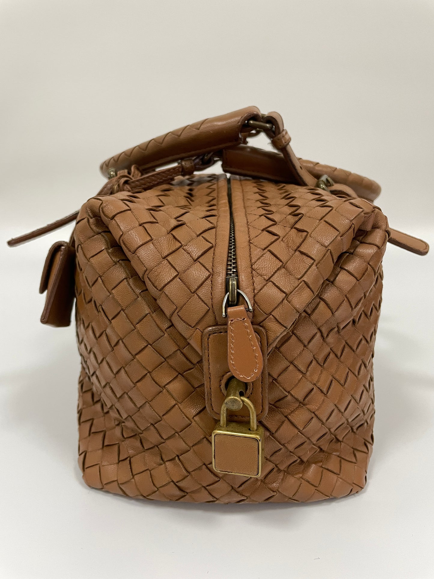 Side view of a Bottega Veneta Intrecciato Montaigne bag in brown leather featuring a zipper and a brass lock detail.