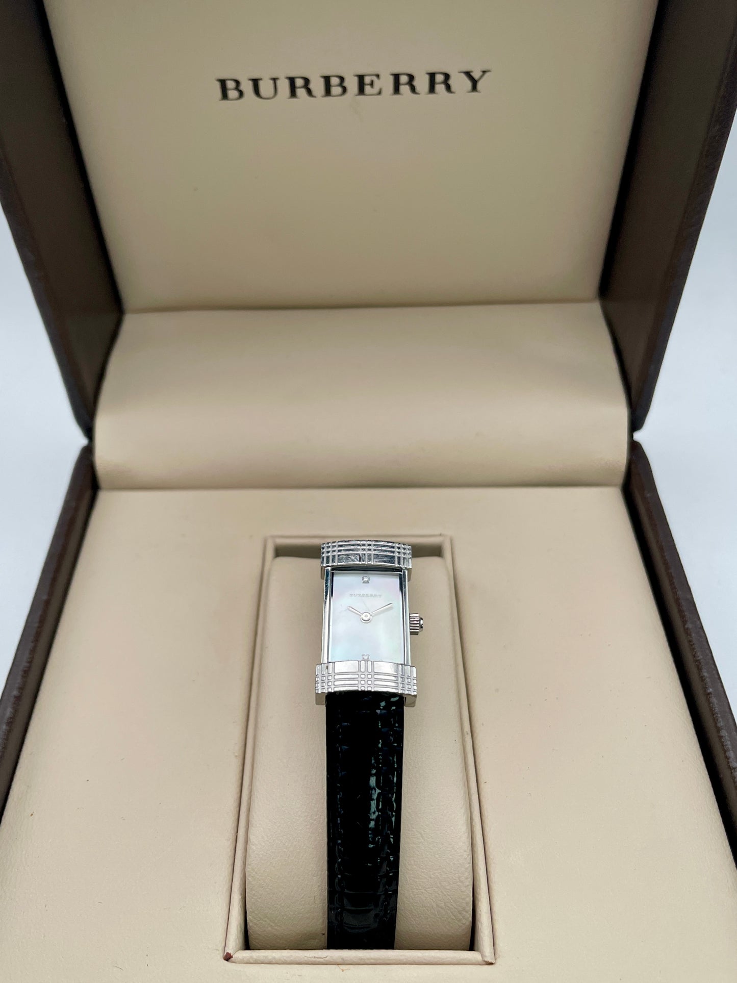 Flat-lay of Burberry watch showing rectangular case, diamond markers, and black strap