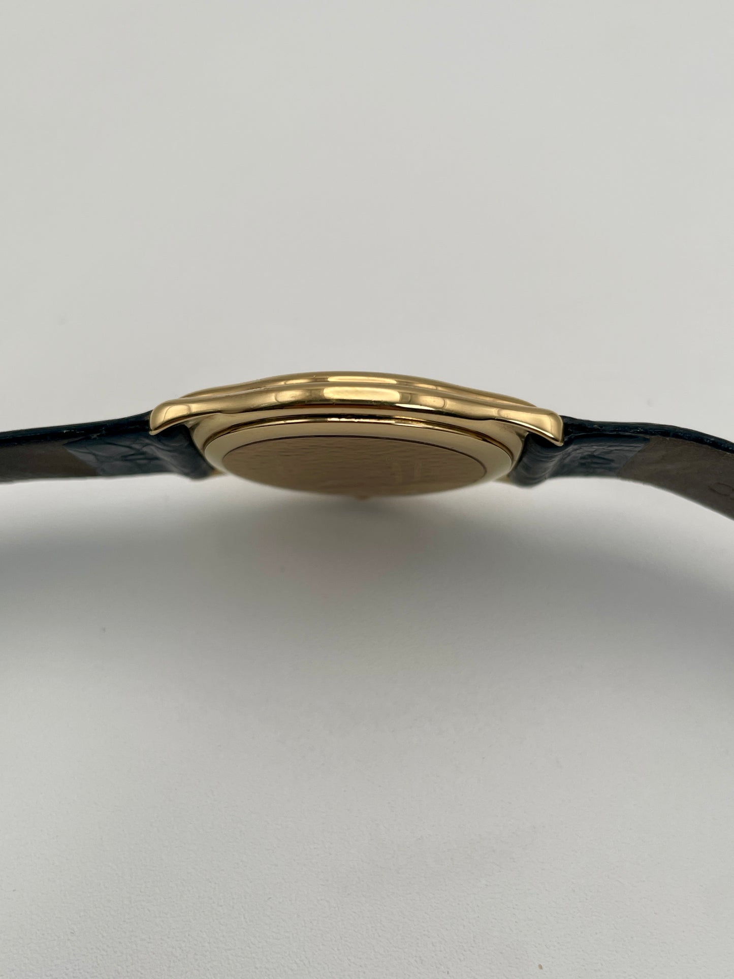 Side view of Christian Dior 3049 gold-tone watch highlighting its sleek case design and black leather strap.