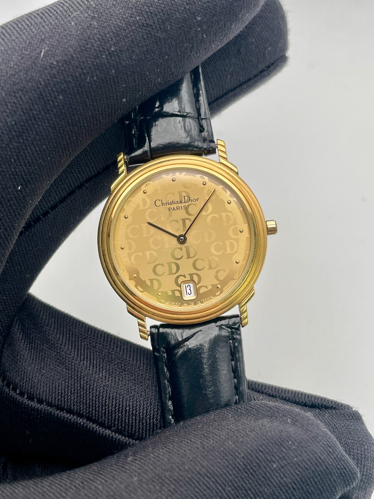 Close-up of the Christian Dior 45.122 watch showing gold-tone CD monogram dial and black strap