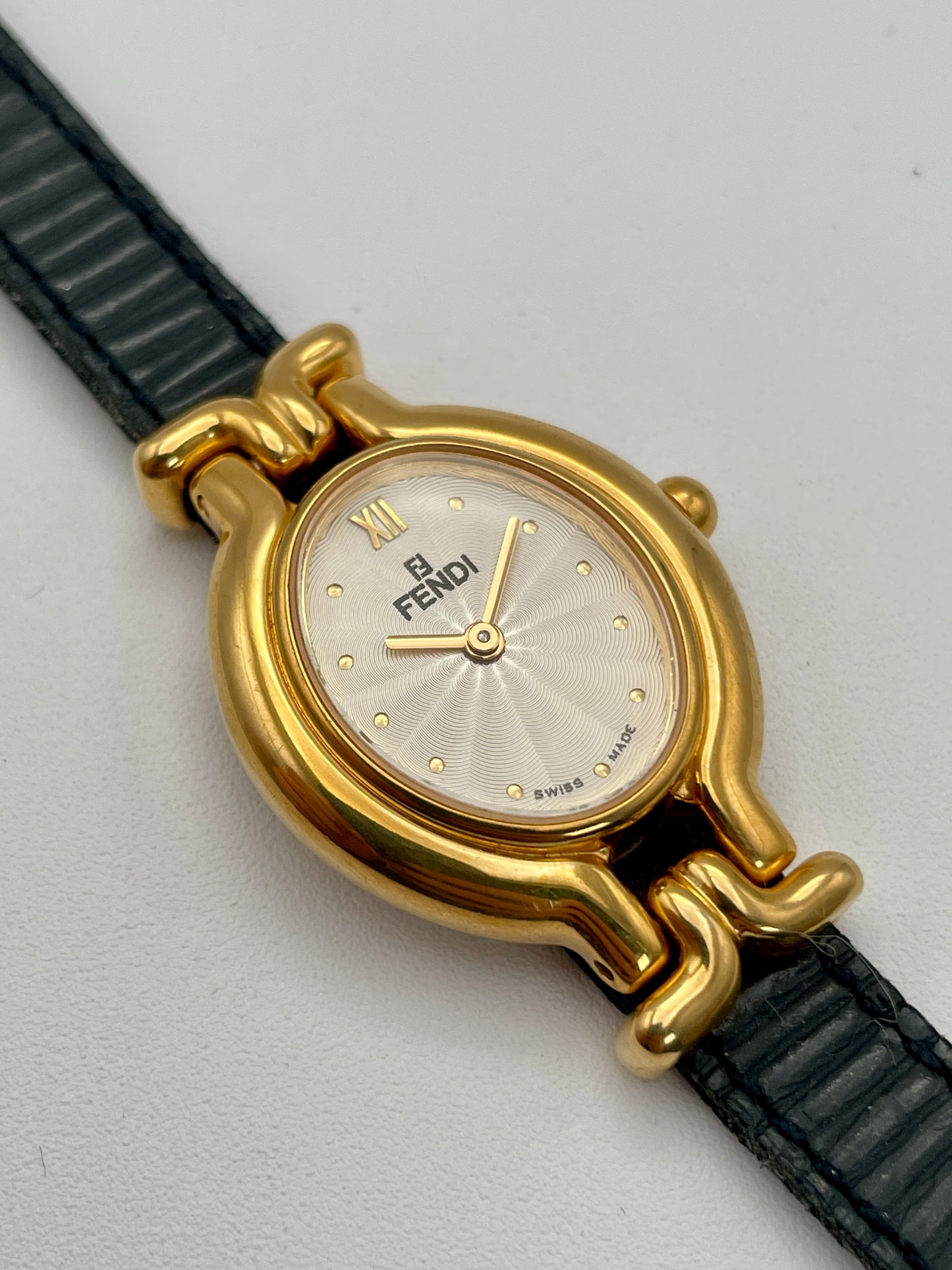 Close front view of Fendi 640L watch with gold case, white dial, and black leather strap.