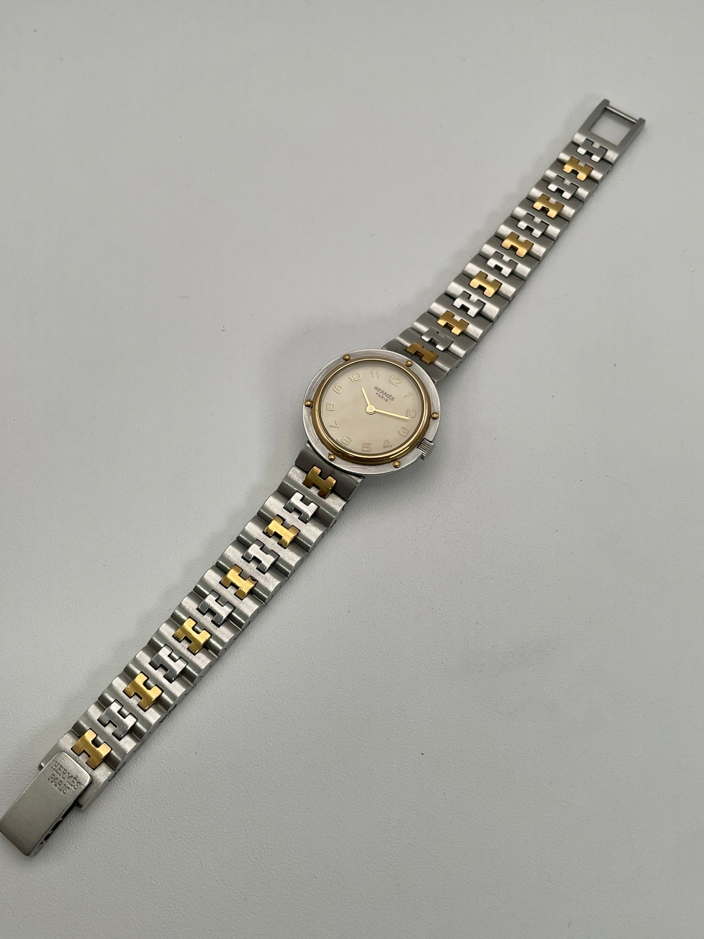 Full bracelet view of Hermès Clipper Olympia watch in stainless steel and gold, showcasing the "H" link bracelet.