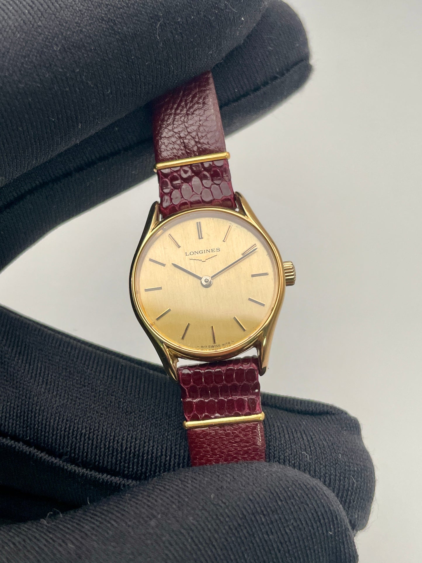 Close-up of the Longines Ref. 4139 vintage women's watch in gold with a burgundy strap, displayed in hand for detail.