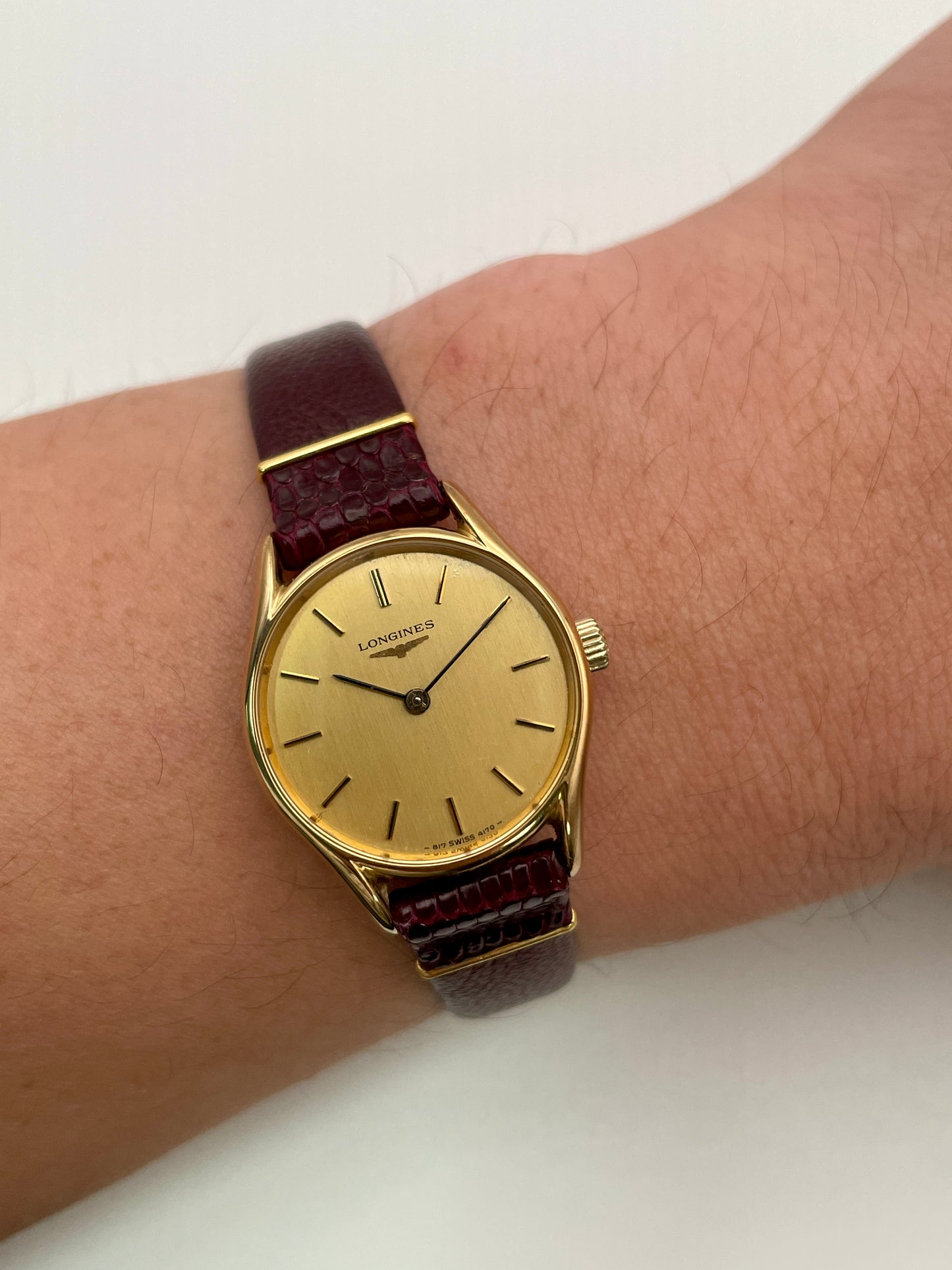 Longines Ref. 4139 vintage women's watch in gold with a burgundy leather strap, styled on the wrist.