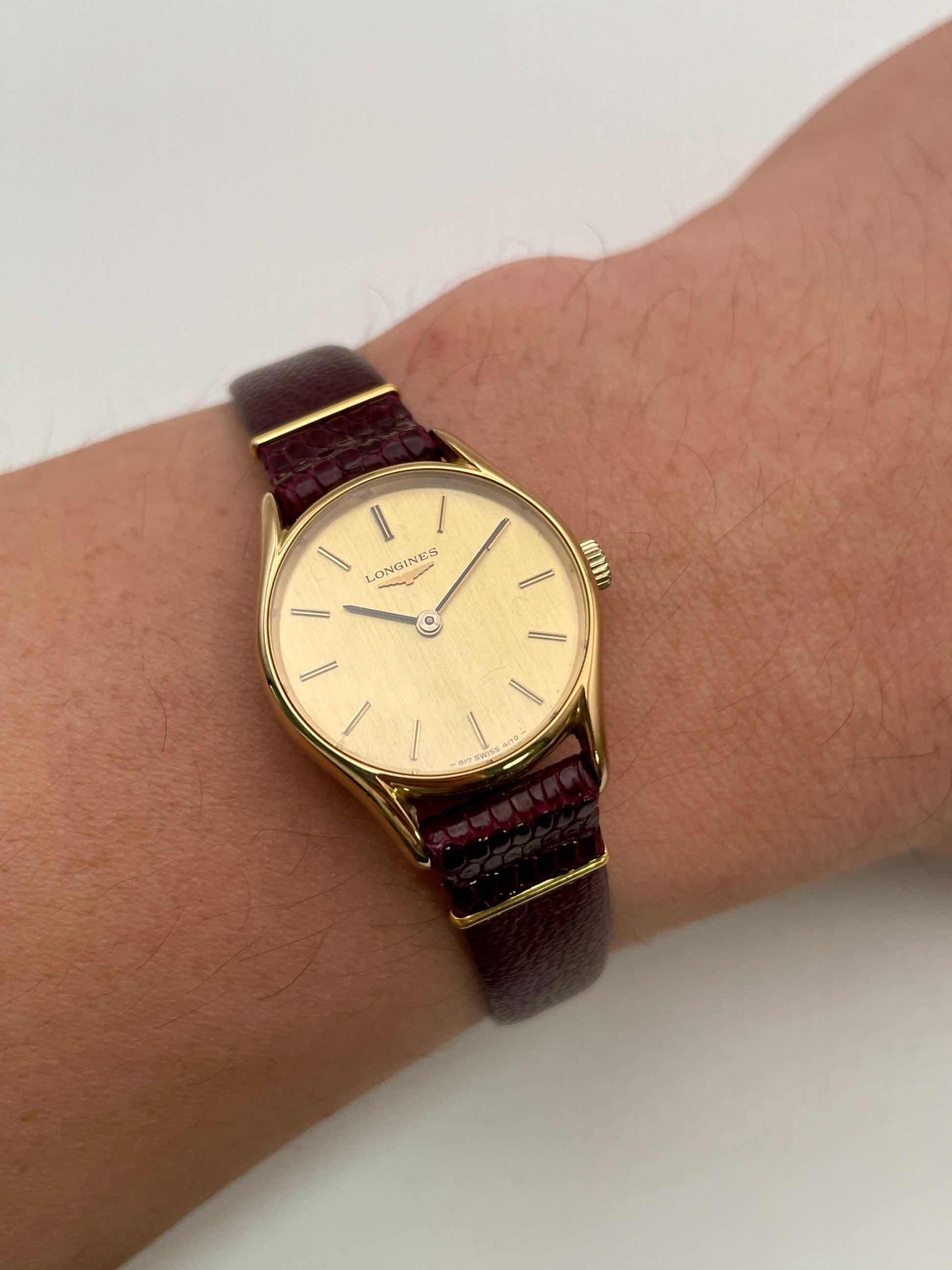 Longines Ref. 4139 vintage women's watch in gold with a burgundy leather strap, styled on the wrist.