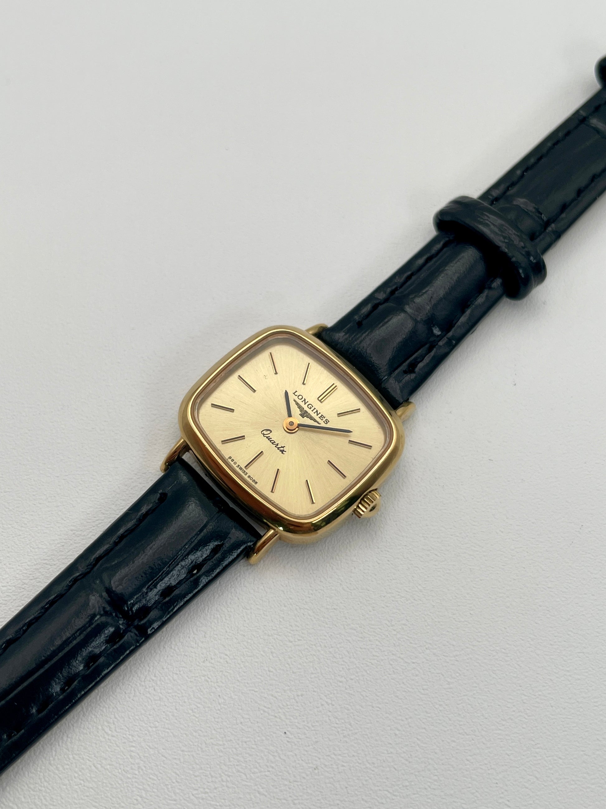 Gold wristwatch with black strap on a light gray background