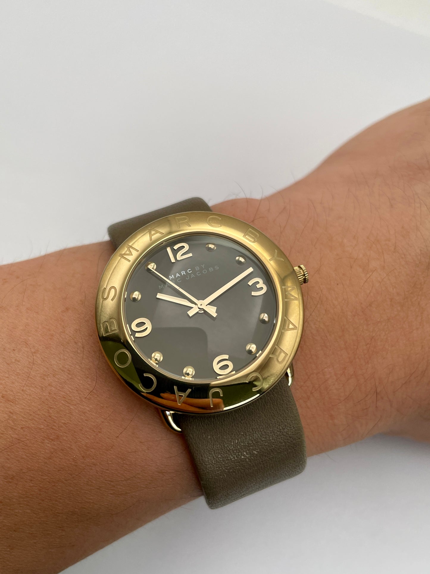 Wrist shot of the Marc by Marc Jacobs watch featuring a gold-tone case, black dial, and tan leather strap