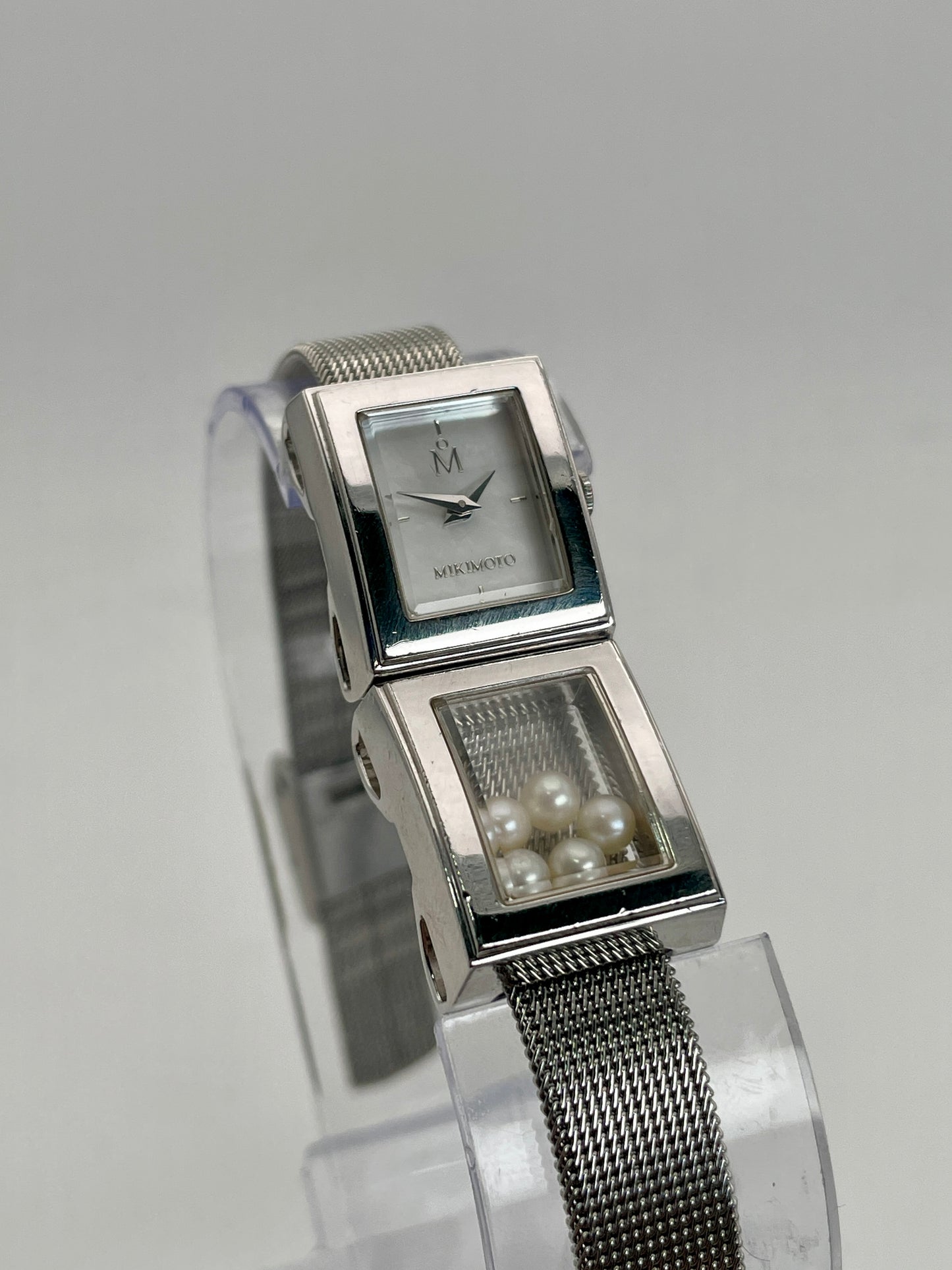 Mikimoto ladies' watch featuring a rectangular silver-tone case, mother-of-pearl dial, and a unique design with a window on the bracelet containing loose pearls.