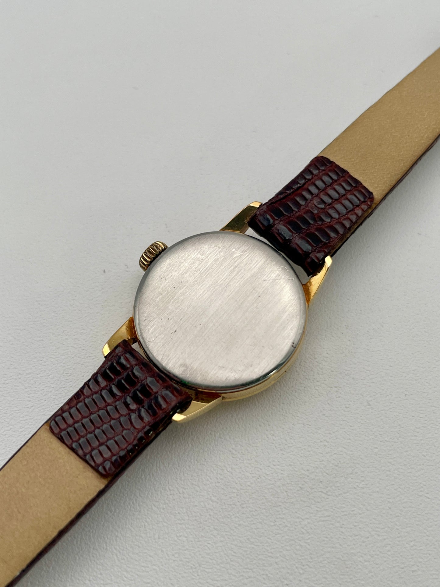 Caseback view of an Omega 511.015 Vintage Women's Watch in gold with a smooth stainless steel back and brown leather strap.