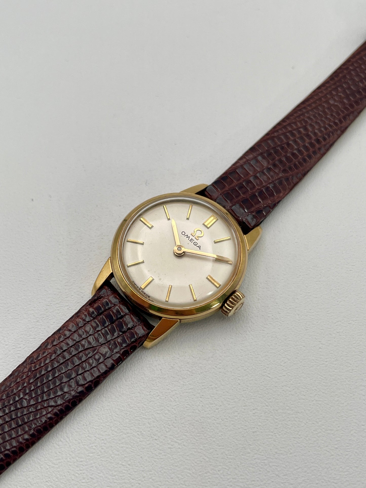Side-angle view of an Omega 511.015 Vintage Women's Watch in gold with a cream dial and textured brown leather strap.