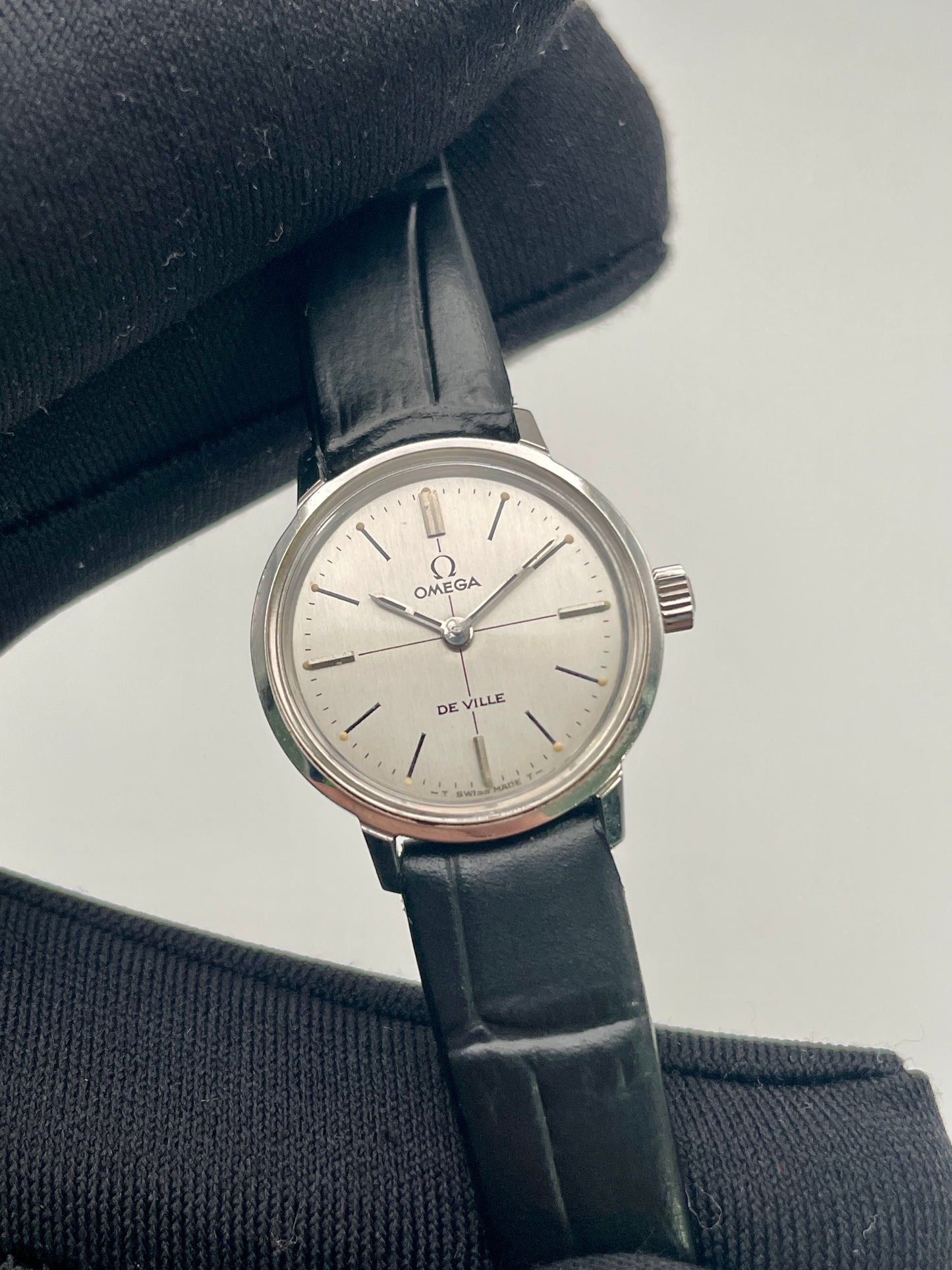 Close-up view of the Omega De Ville 515.007 vintage watch, highlighting its silver sunburst dial, minimalist markers, and sleek black strap.