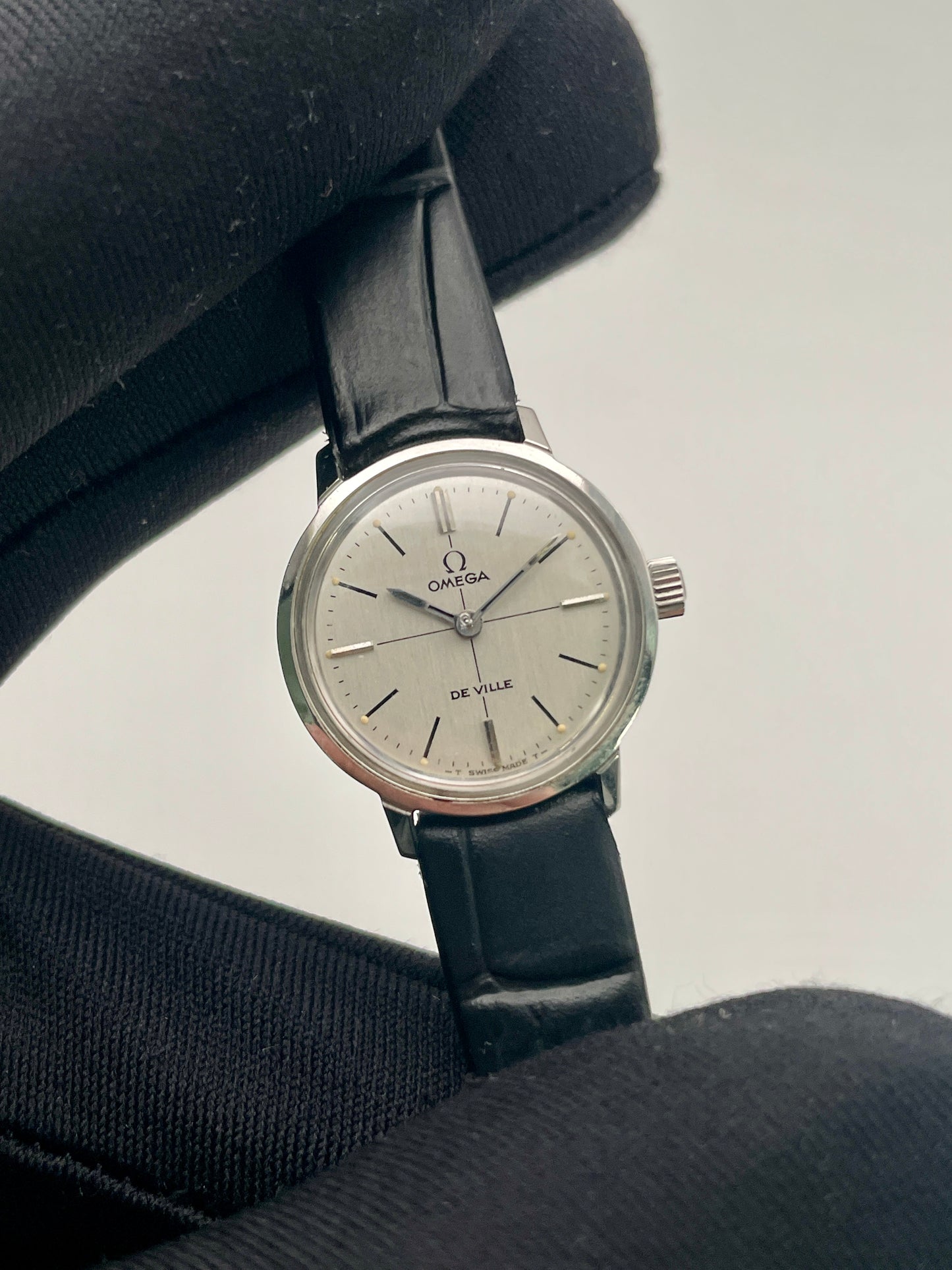 Close-up view of the Omega De Ville 515.007 vintage watch, highlighting its silver sunburst dial, minimalist markers, and sleek black strap.