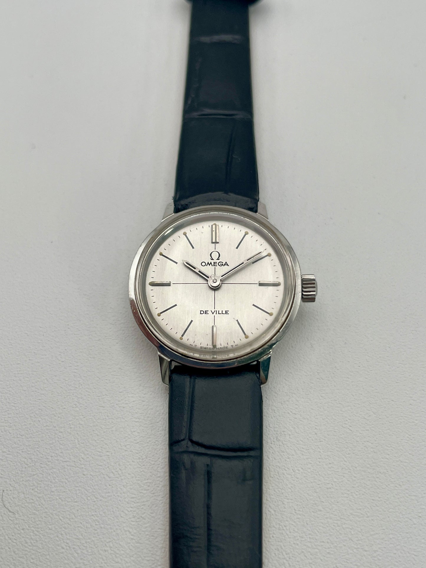 Front view of the Omega De Ville 515.007 vintage women's watch in stainless steel, showcasing a silver sunburst dial with minimalist hour markers and a black leather strap.