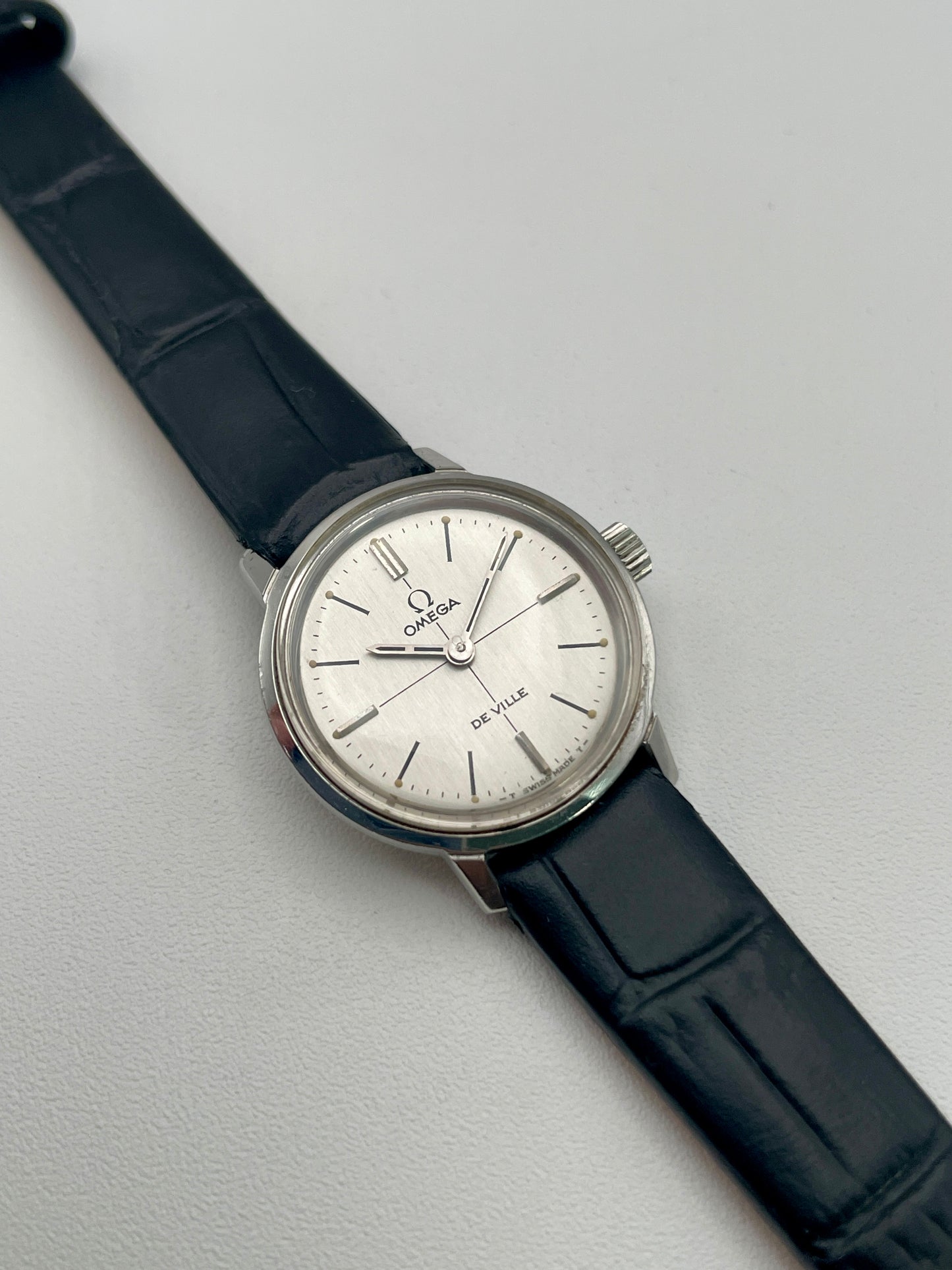 Main view of the Omega De Ville 515.007 vintage women's watch in stainless steel, showcasing a silver sunburst dial with minimalist hour markers and a black leather strap.