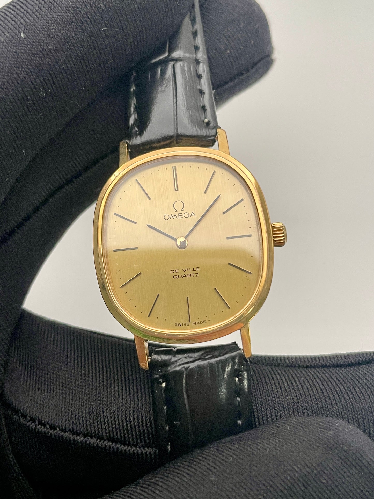 Close-up view of the Omega De Ville Oval watch, emphasizing the gold-tone case and champagne dial.