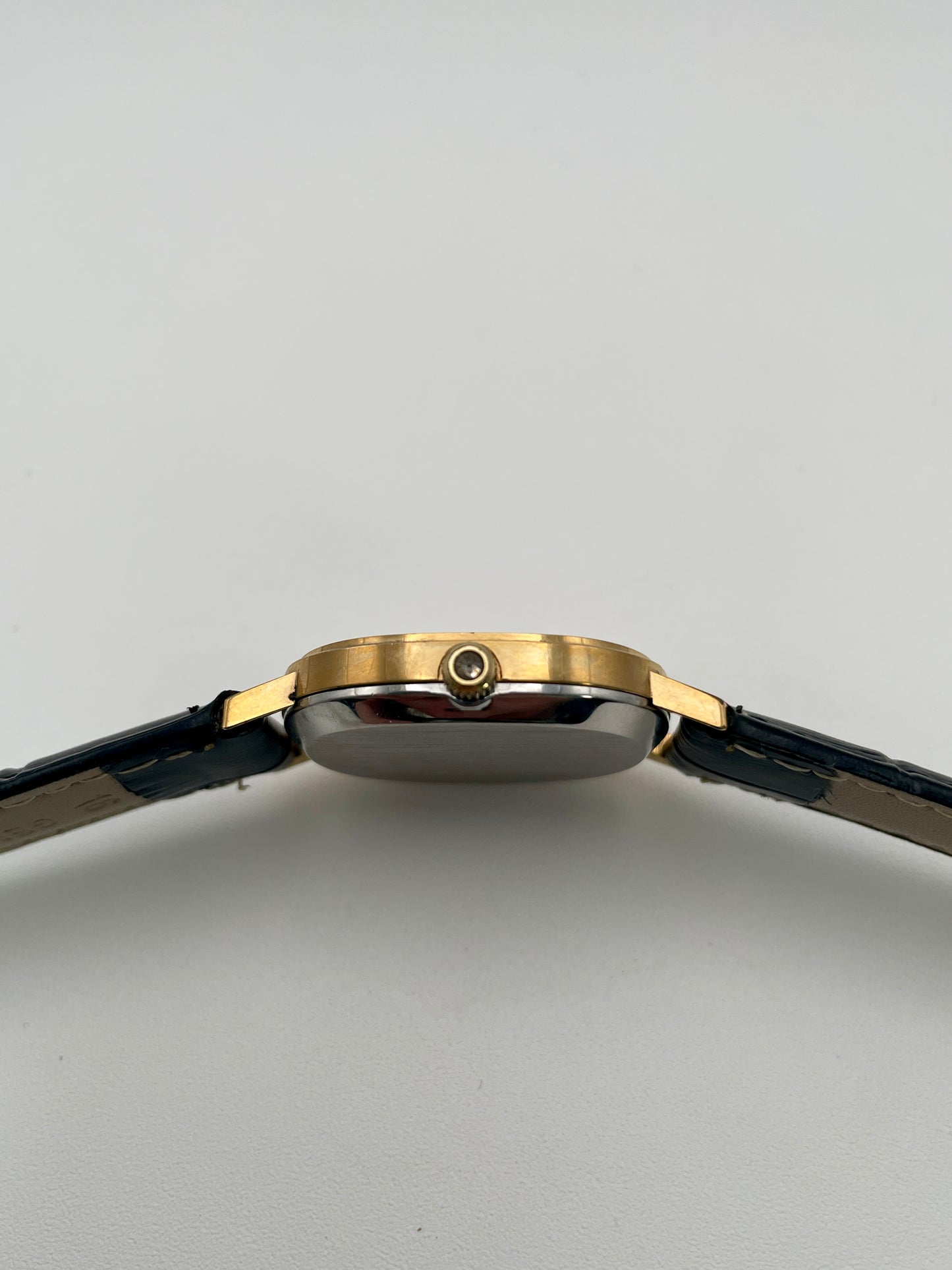 Omega De Ville Oval watch side view, highlighting the gold case and unique push button crown.
