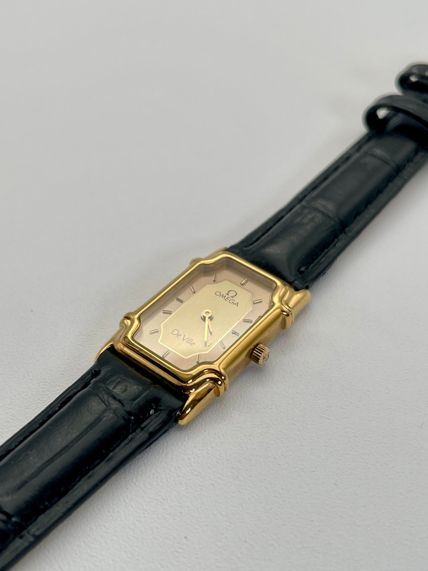 Diagonal view of the Omega De Ville "Challenge" watch with an Art Deco style gold case, highlighting the sector two-tone rectangular dial and gold-tone hands.