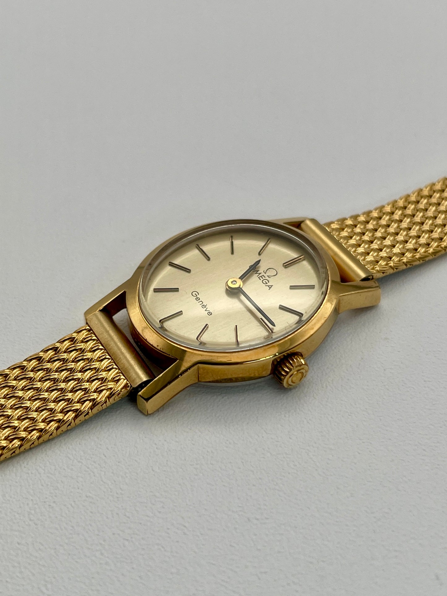 Omega Genève oval ladies watch in gold with a mesh bracelet, diagonal view.