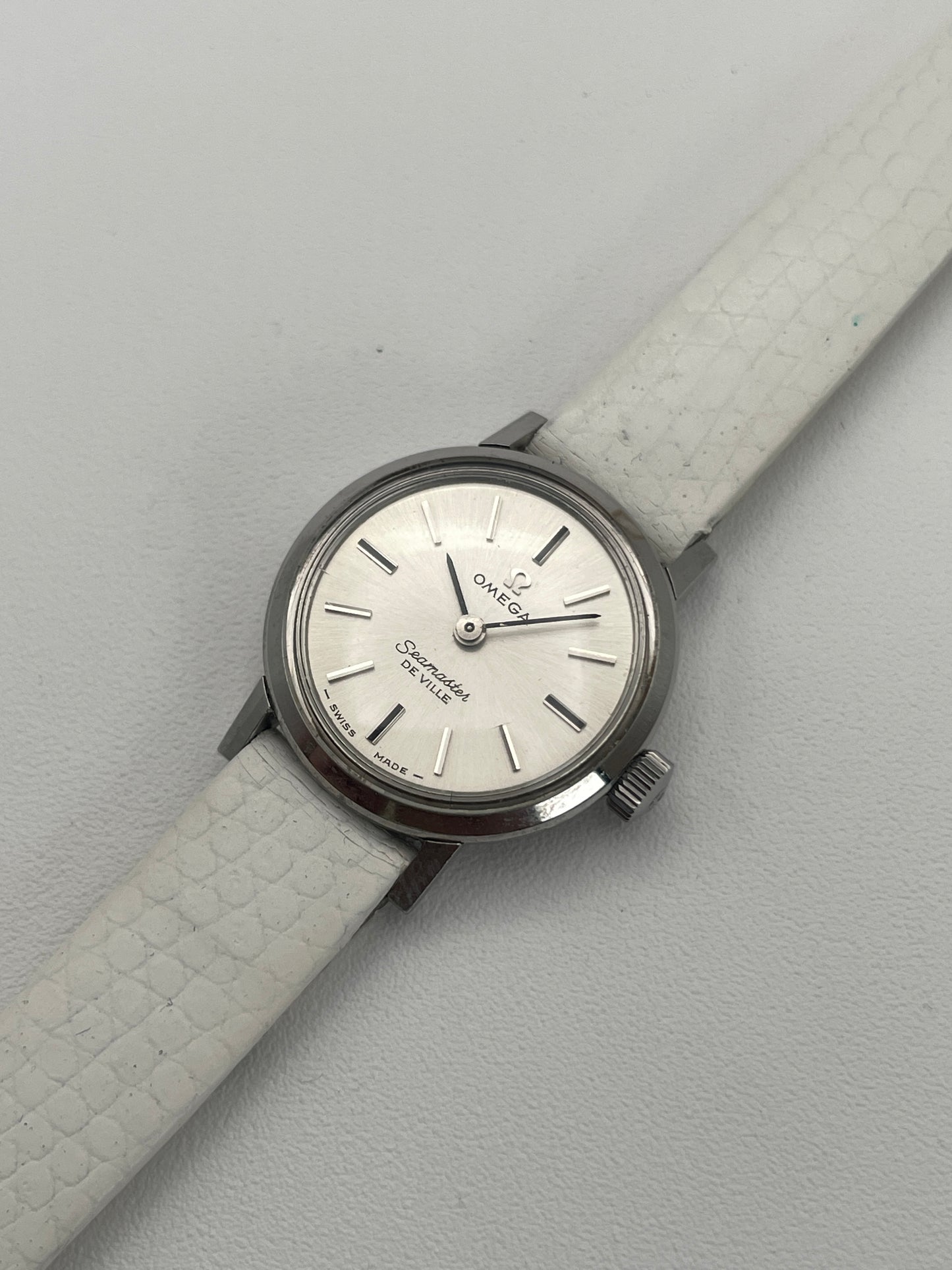 Diagonal view of an Omega Seamaster De Ville ladies watch, displaying its sleek silver dial and textured white leather strap.