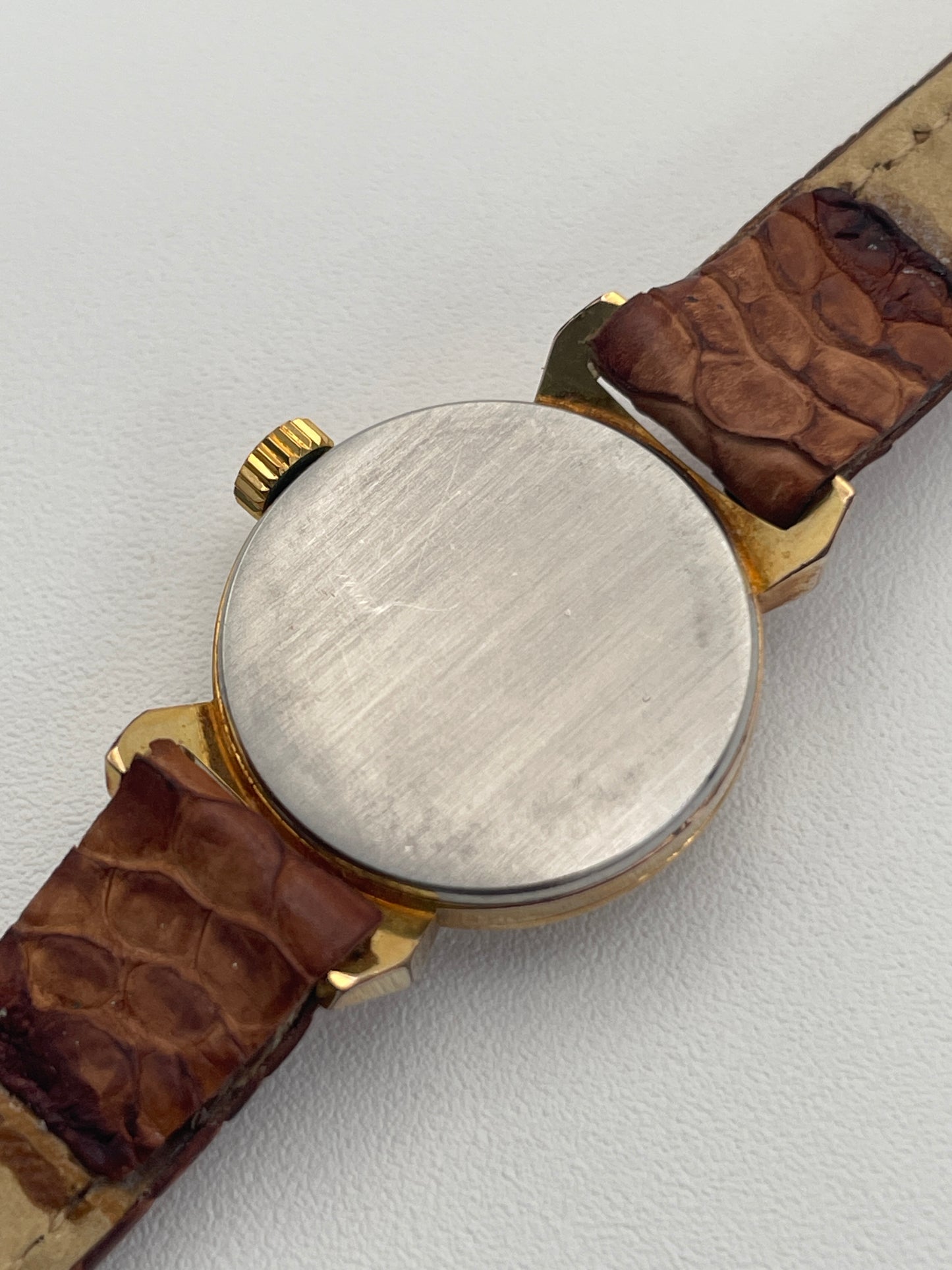 Caseback view of a vintage Omega ladies watch with gold bullhorn lugs and a tan leather strap.