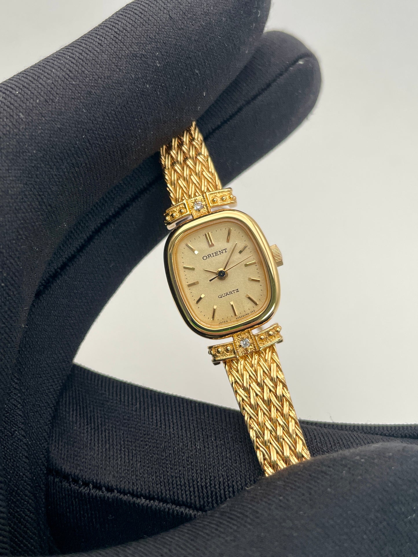 Close-up view of Orient Vintage Women's Watch held in a black glove, highlighting its gold finish and intricate bracelet.