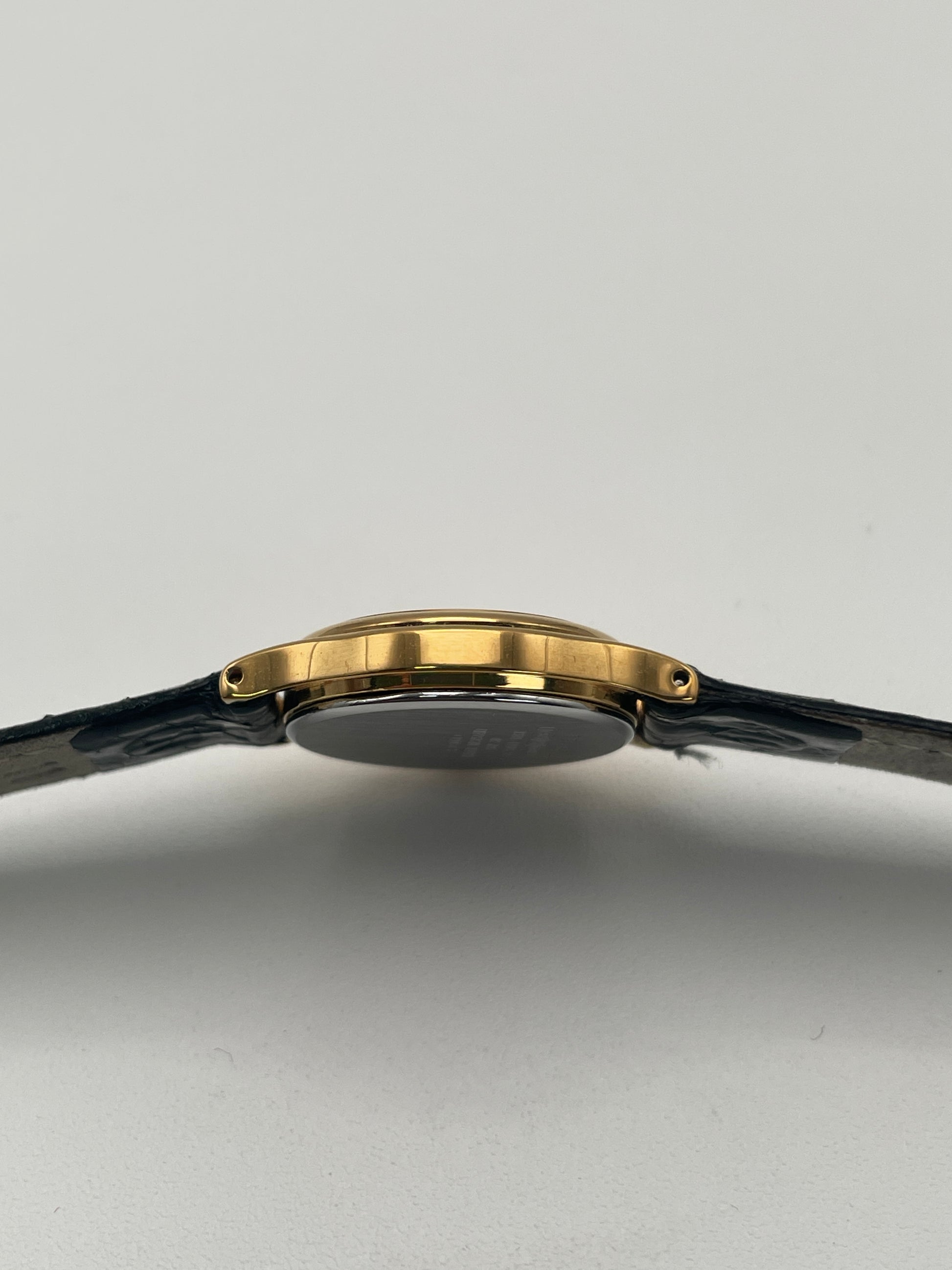 Side view of Seiko Exceline gold watch with a black leather strap and textured dial.