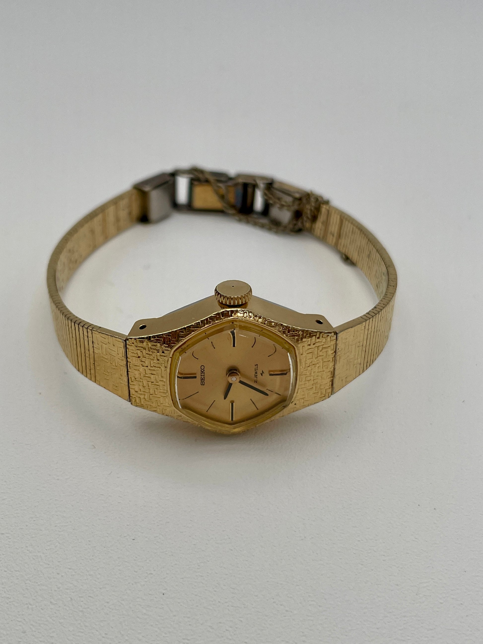 Flat lay angled view of a vintage Seiko ladies' watch, displaying its gold-tone textured case, bracelet, and minimalist gold dial with black hour markers and hands.