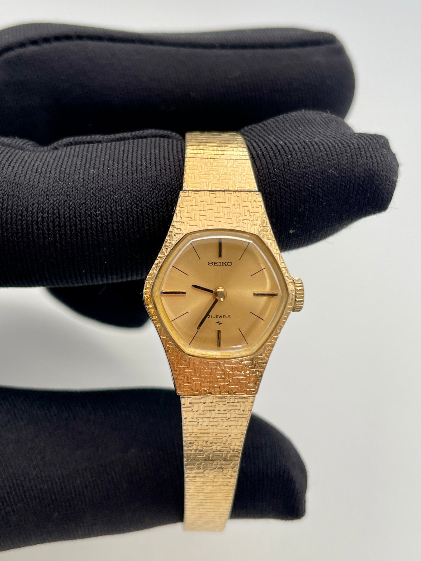Close-up view of a vintage Seiko ladies' watch with a gold-tone textured case and bracelet, featuring a simple gold dial with thin black hour markers and hands.
