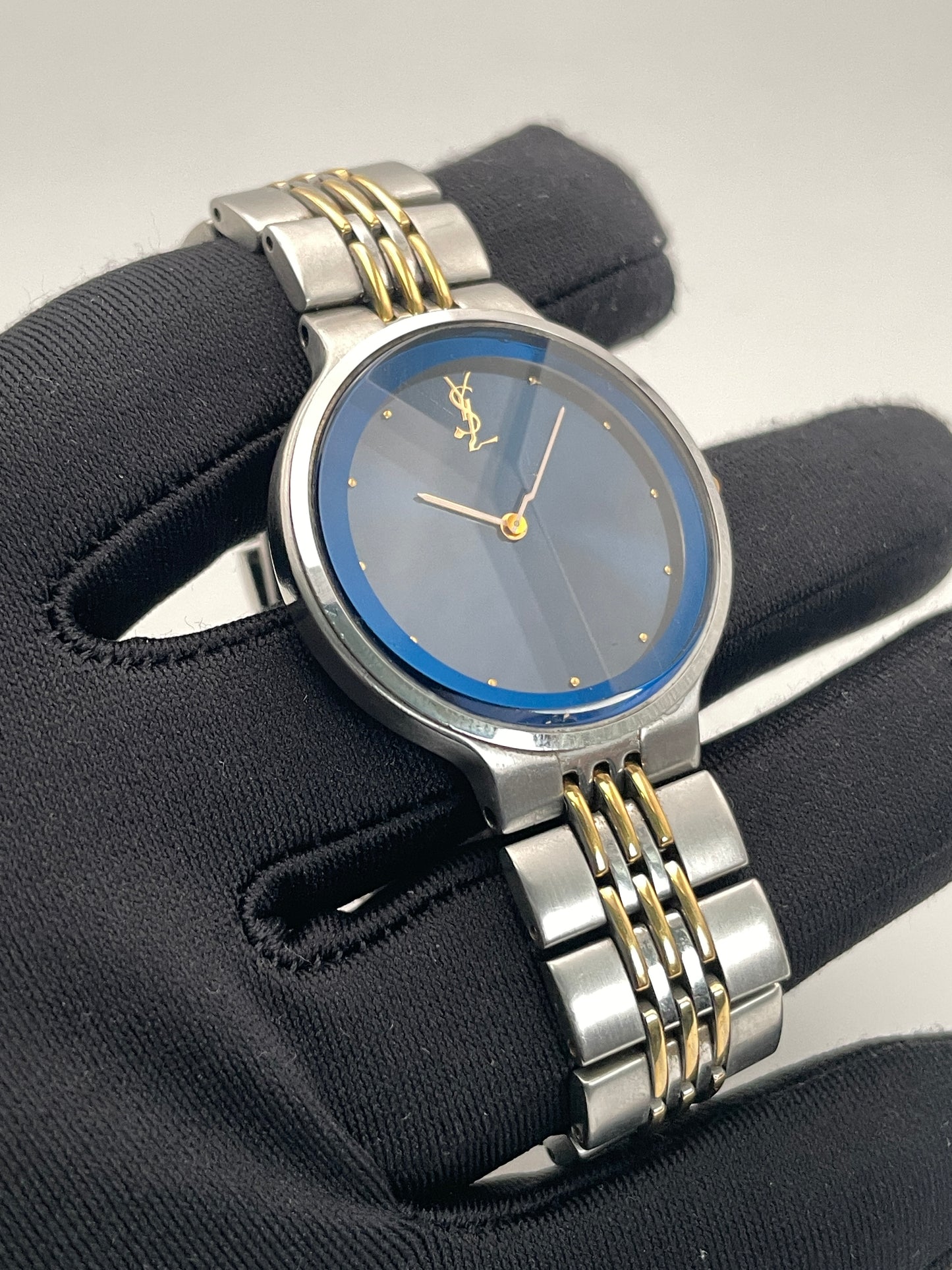 Handheld close-up of the YSL La Collection vintage women's watch with a faceted crystal and blue sunray dial.