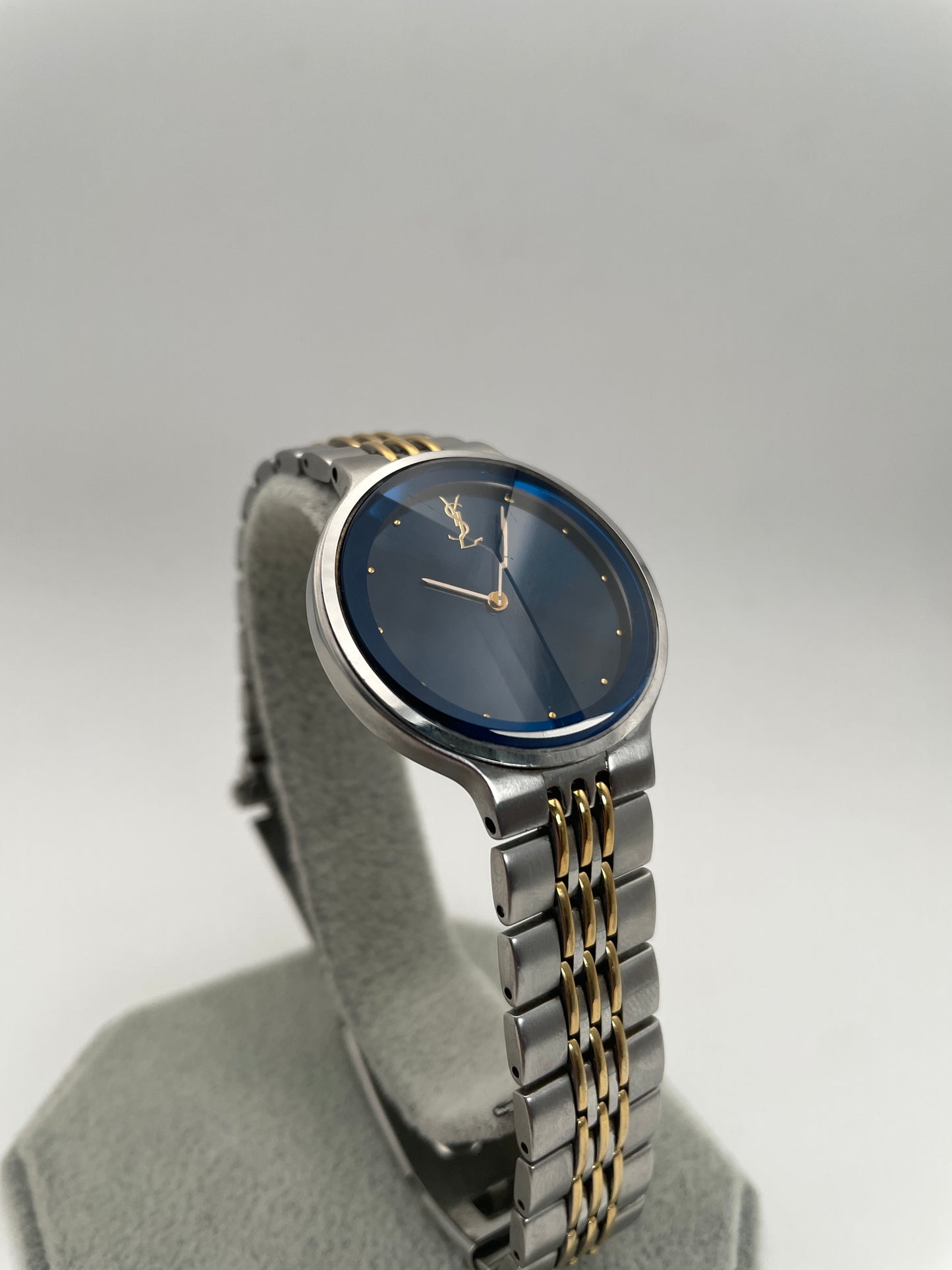 YSL La Collection vintage women's watch with a blue sunray dial, faceted crystal, and a stainless steel and gold-tone bracelet, displayed upright on a stand.