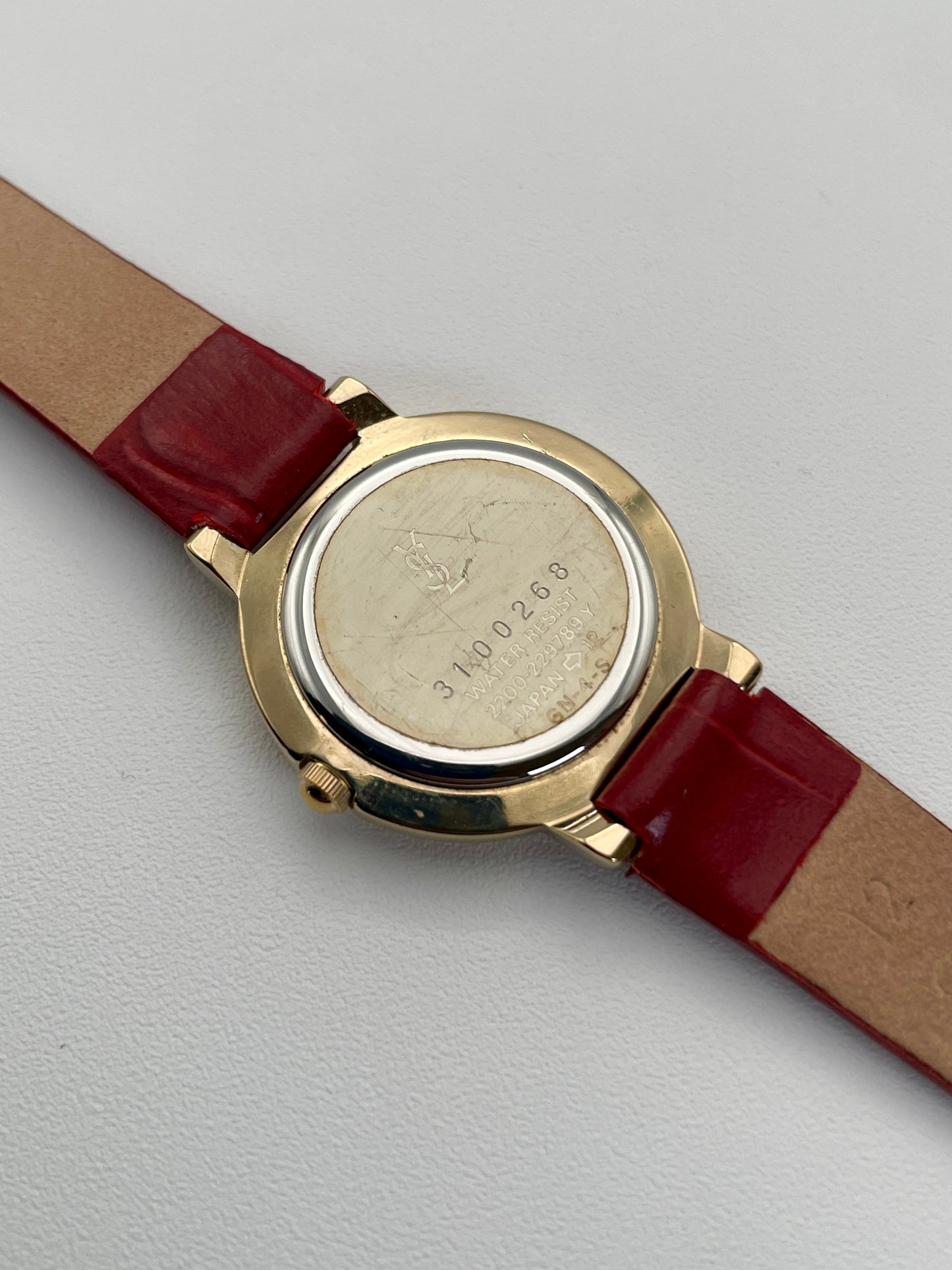 Caseback view of the Yves Saint Laurent Pour Femme watch with a gold case and red leather strap, showing the engraved caseback with the YSL logo.