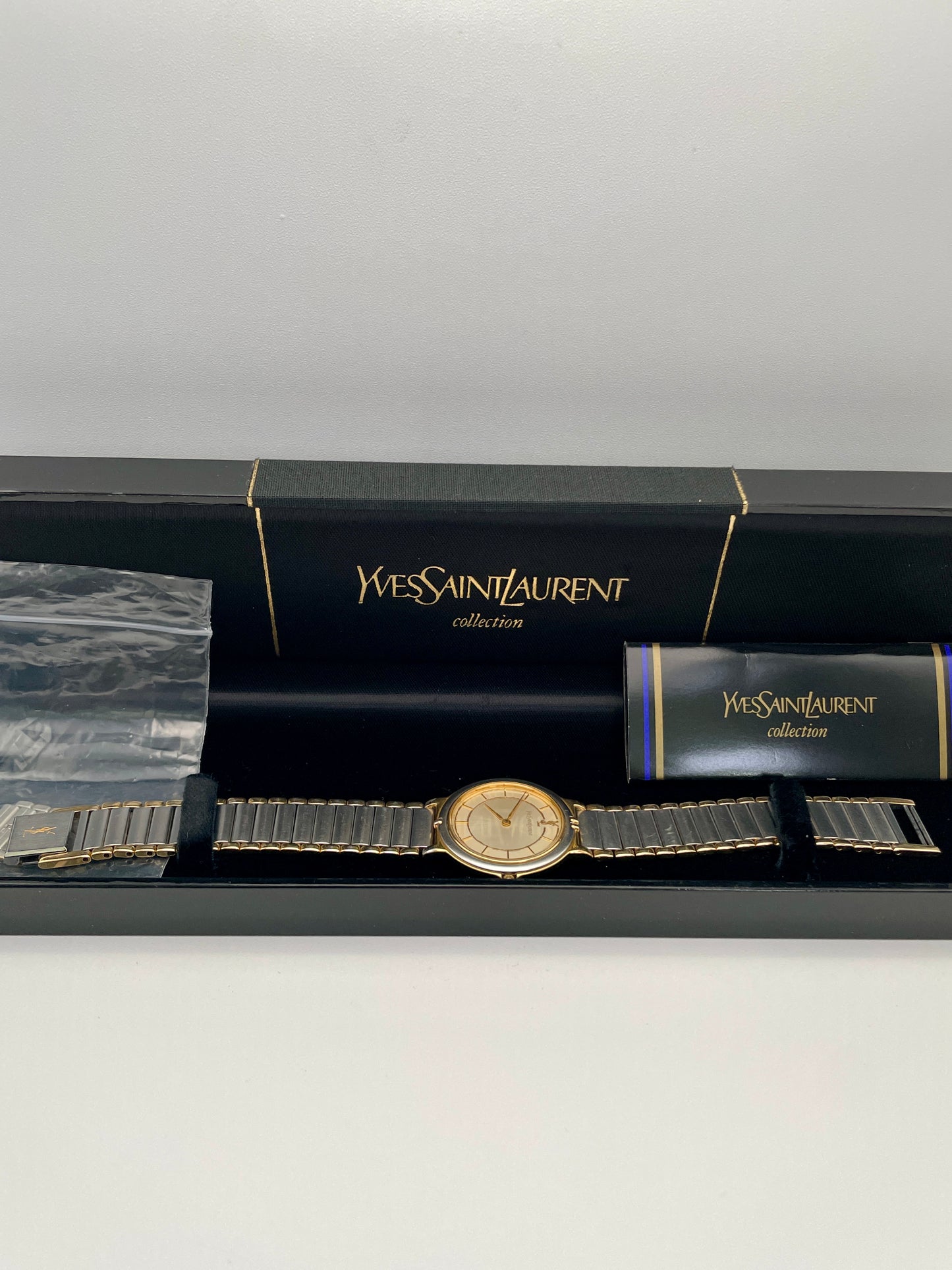 Full view of the Vintage Yves Saint Laurent two-tone watch with a gold and silver-tone bracelet laid flat shown with its complete inclusions and box.