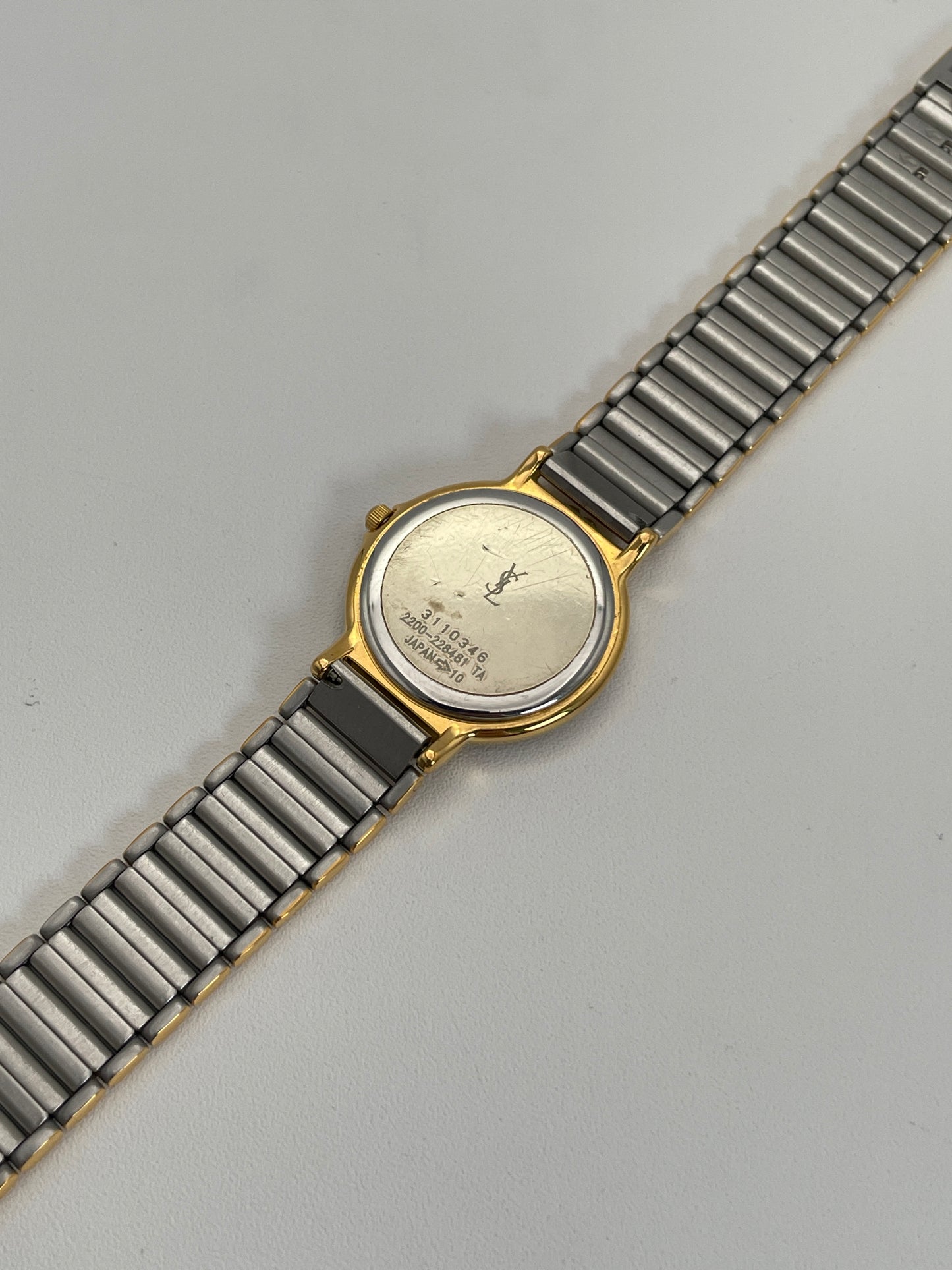 Full caseback view of a YSL vintage two-tone watch with a silver dial, gold accents, and a metal bracelet with gold and silver links highlighting the engraved caseback.