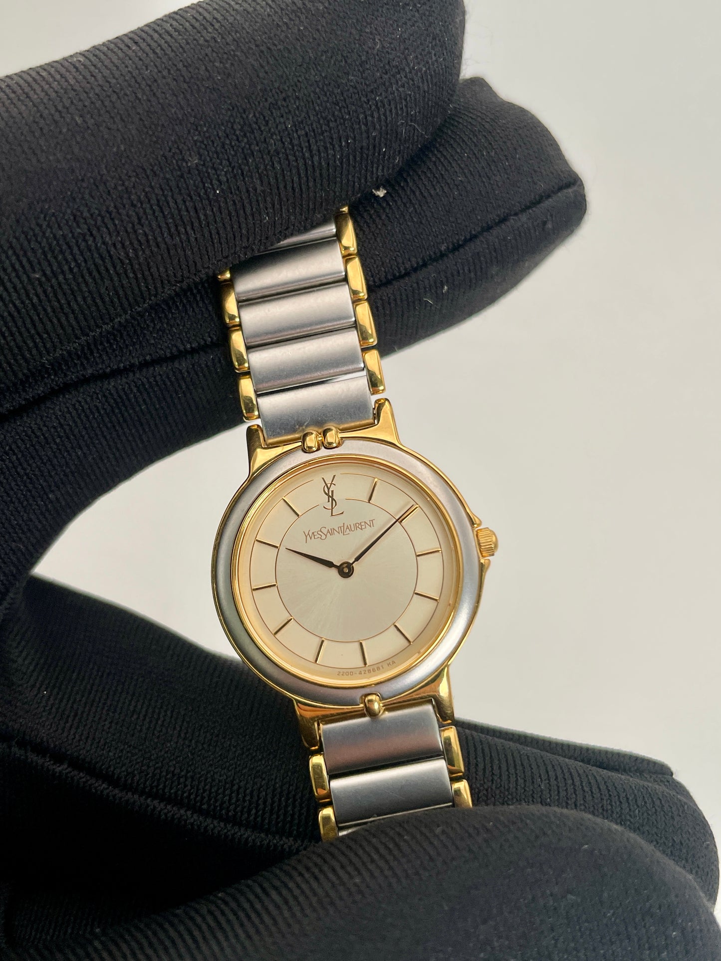 Close-up view of a YSL vintage two-tone watch held in a gloved hand, focusing on the silver dial with gold accents and two-tone metal bracelet.