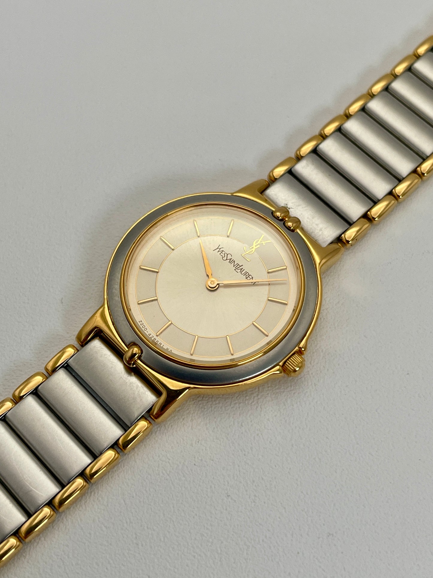 Diagonal view of a YSL vintage two-tone watch showcasing its elegant silver dial with gold hands and a two-tone bracelet.