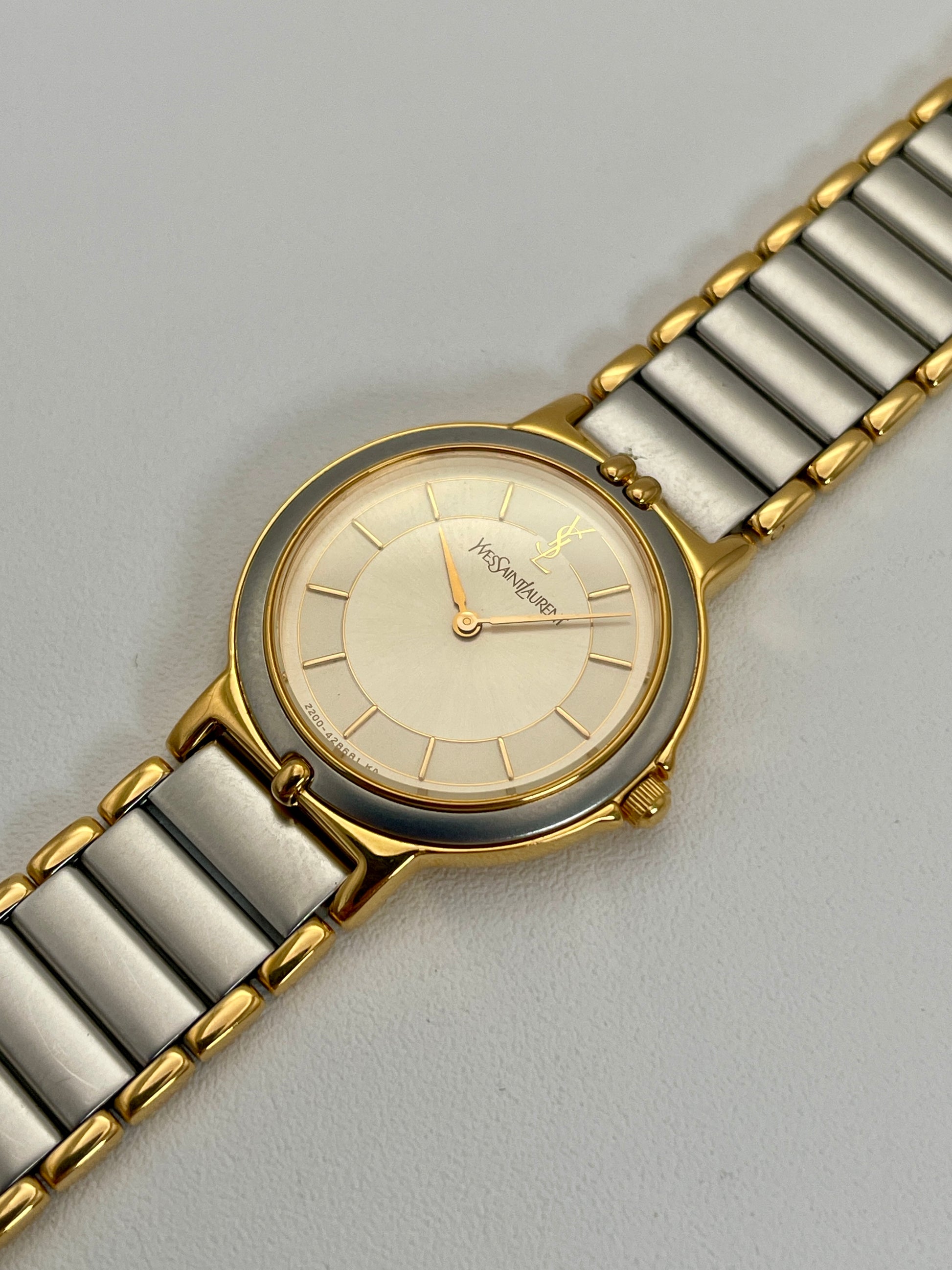 Diagonal view of a YSL vintage two-tone watch showcasing its elegant silver dial with gold hands and a two-tone bracelet.