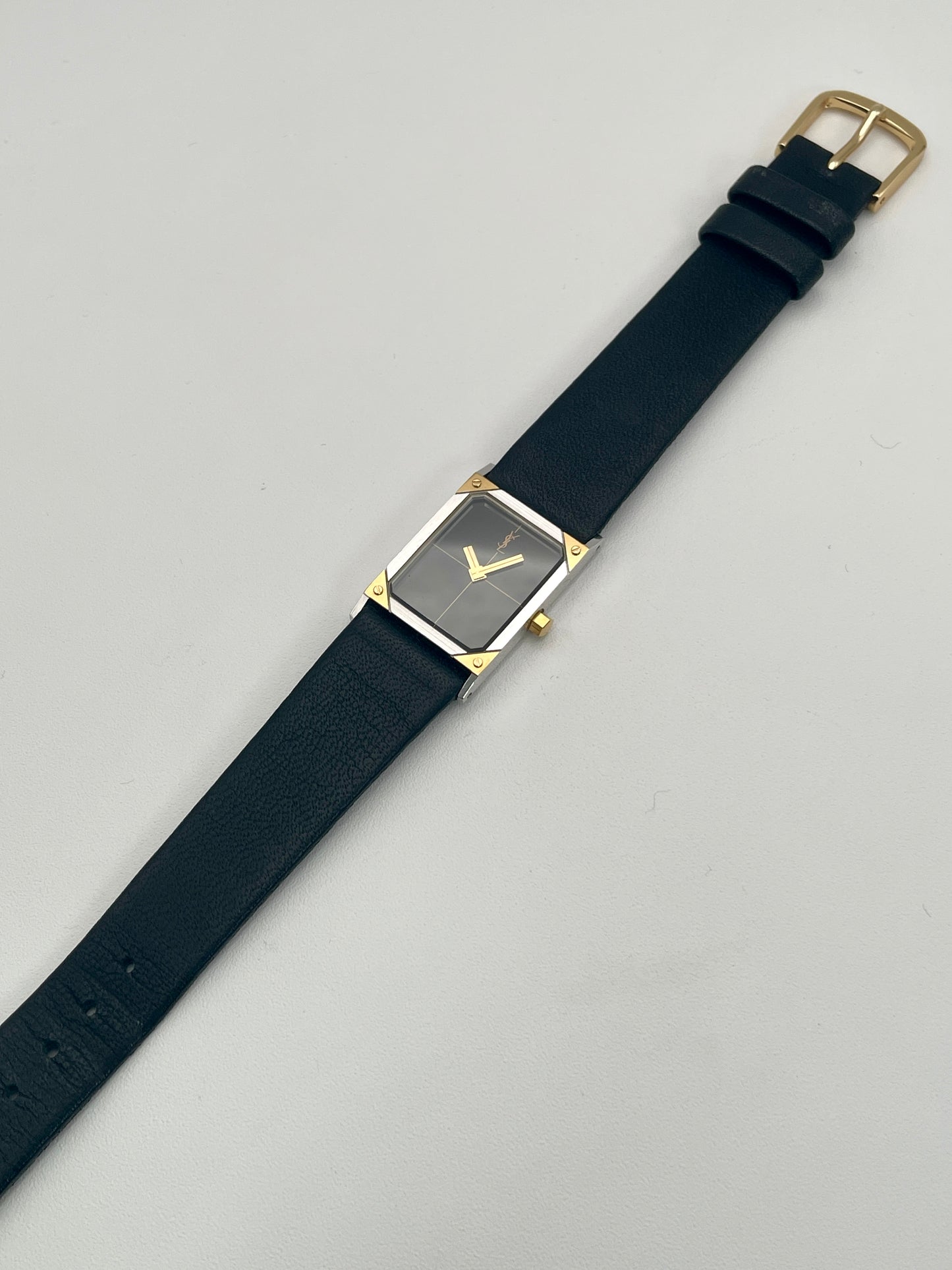 Yves Saint Laurent vintage women's watch laid flat, showing the black leather strap and steel and gold case.