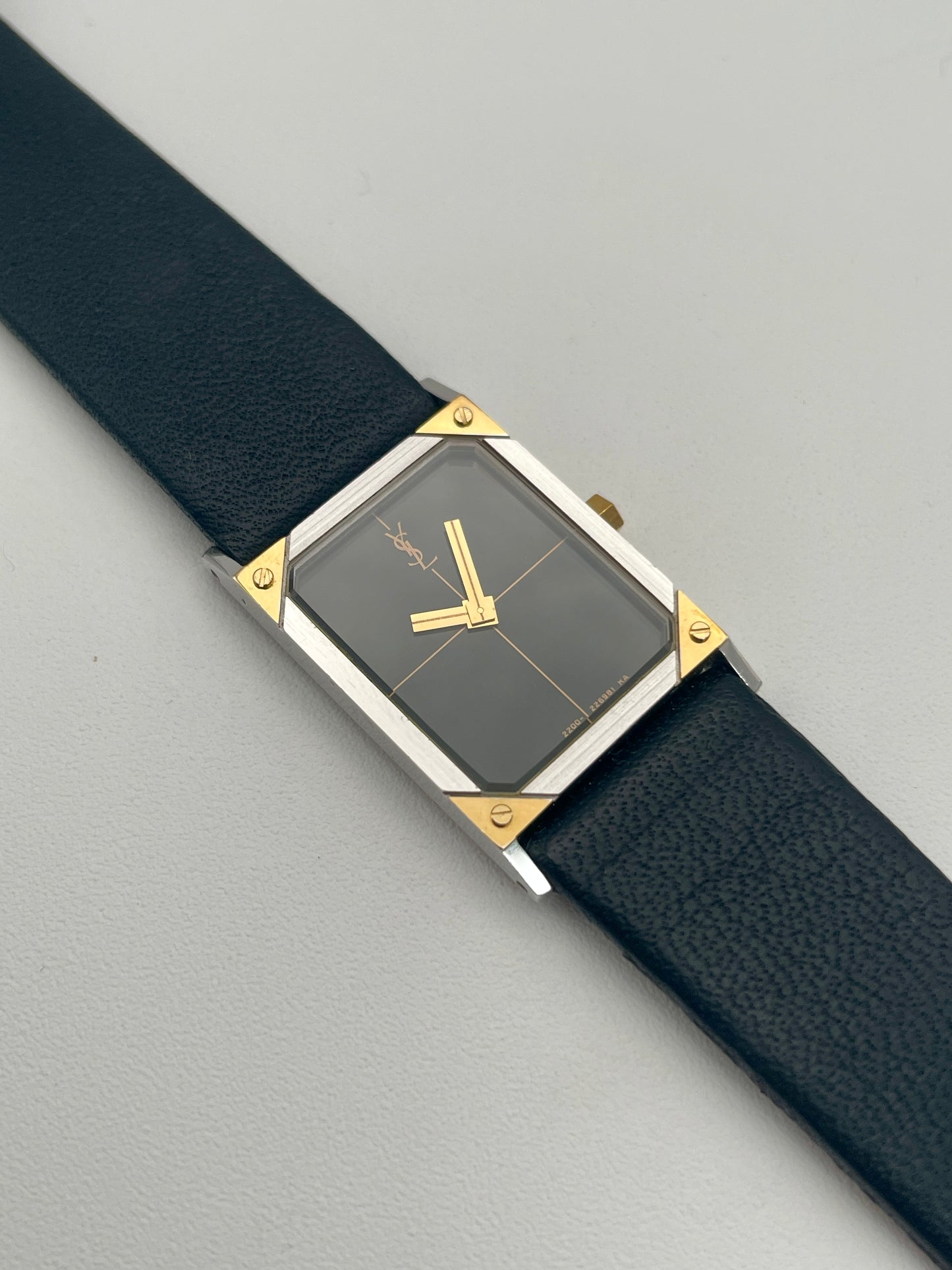 Front view of Yves Saint Laurent vintage women's watch with a steel and gold rectangular case and black leather strap.