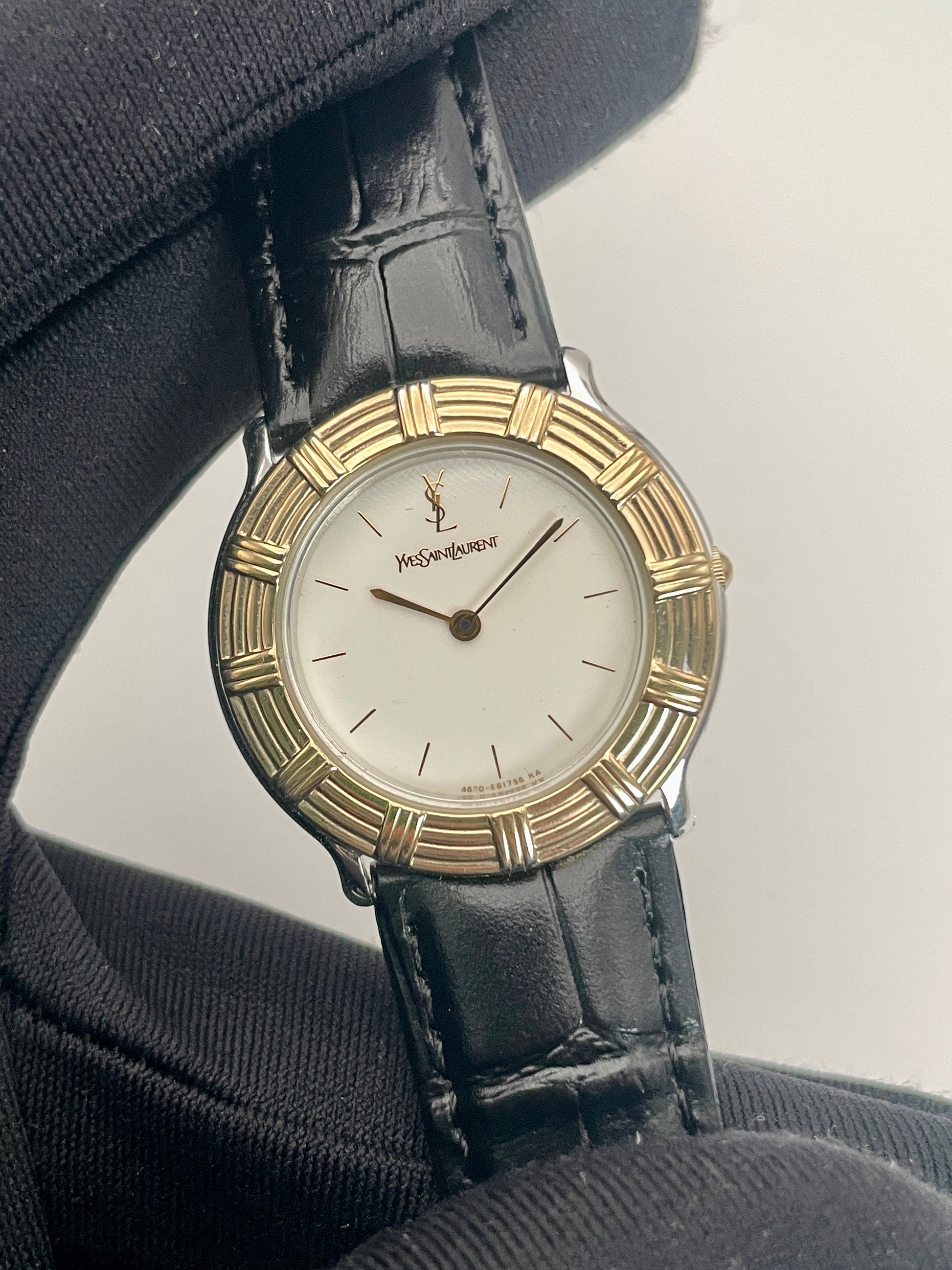 Close-up view of Yves Saint Laurent vintage watch, highlighting its gold-tone bezel and white dial.