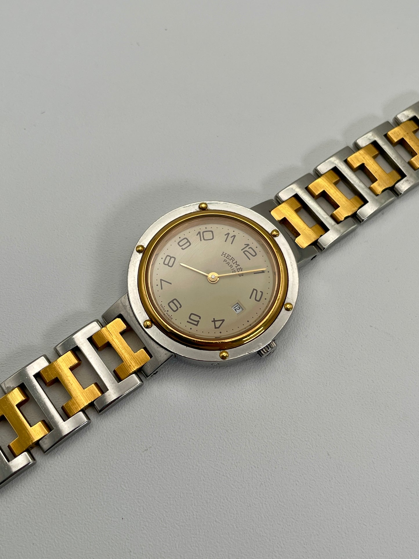 Diagonal view of a Hermes Clipper 30mm two-tone watch, highlighting the silver dial, Arabic numerals, and the stainless steel and gold bracelet.