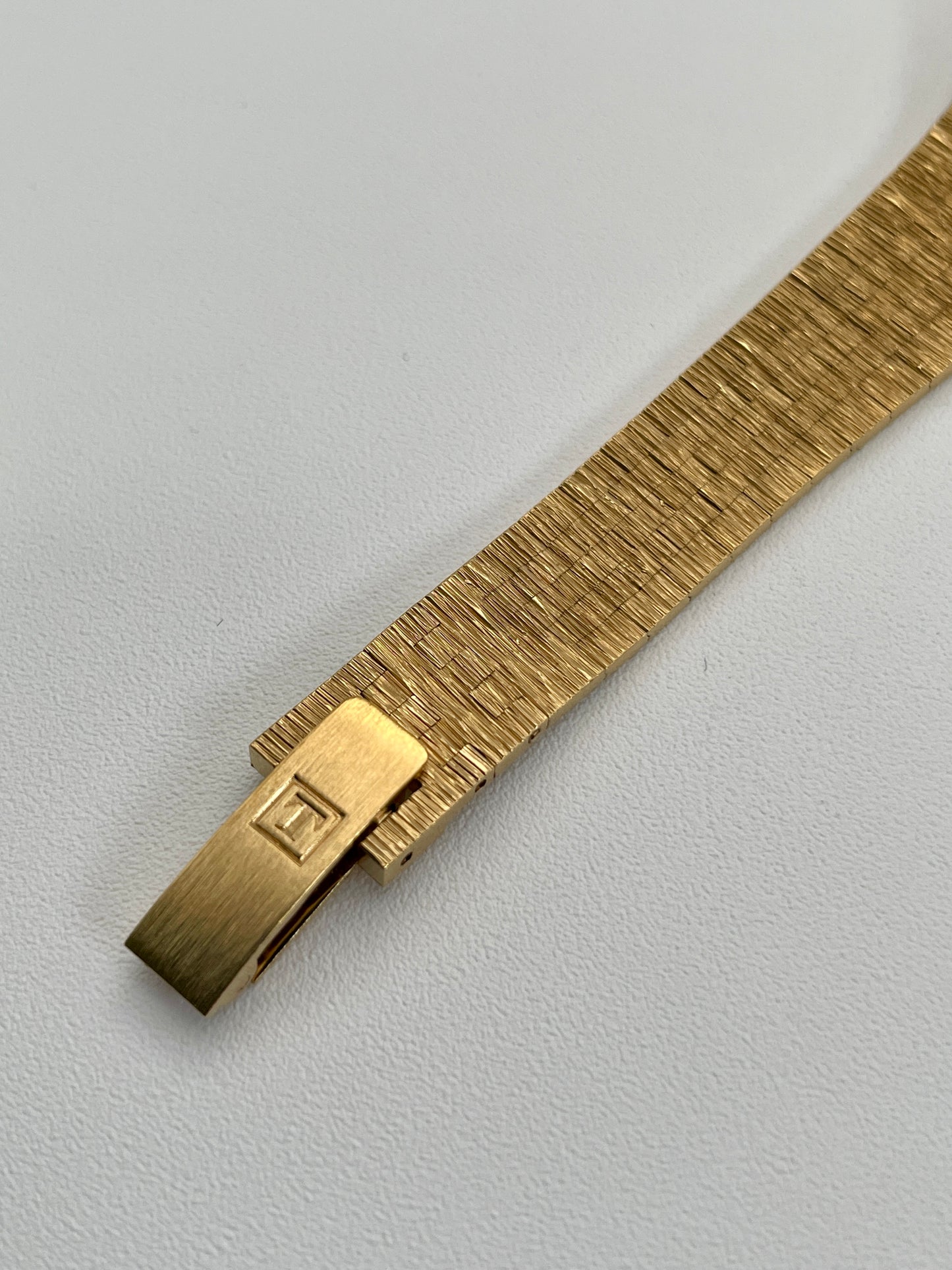 View of the buckle on the Tissot Stylist gold dress watch with a textured gold-tone design matching the integrated bracelet