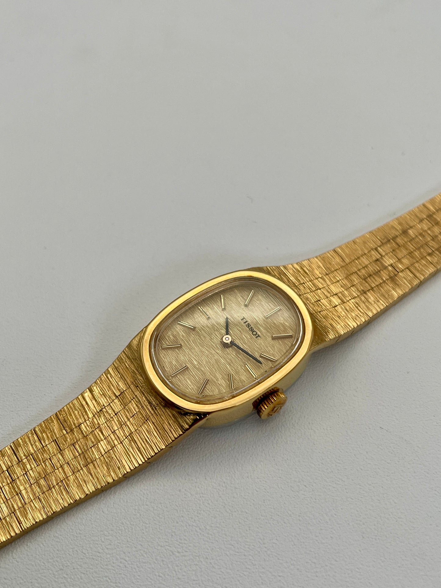 Diagonal view of a Tissot Stylist gold dress watch highlighting the textured gold-tone oval case and integrated bracelet