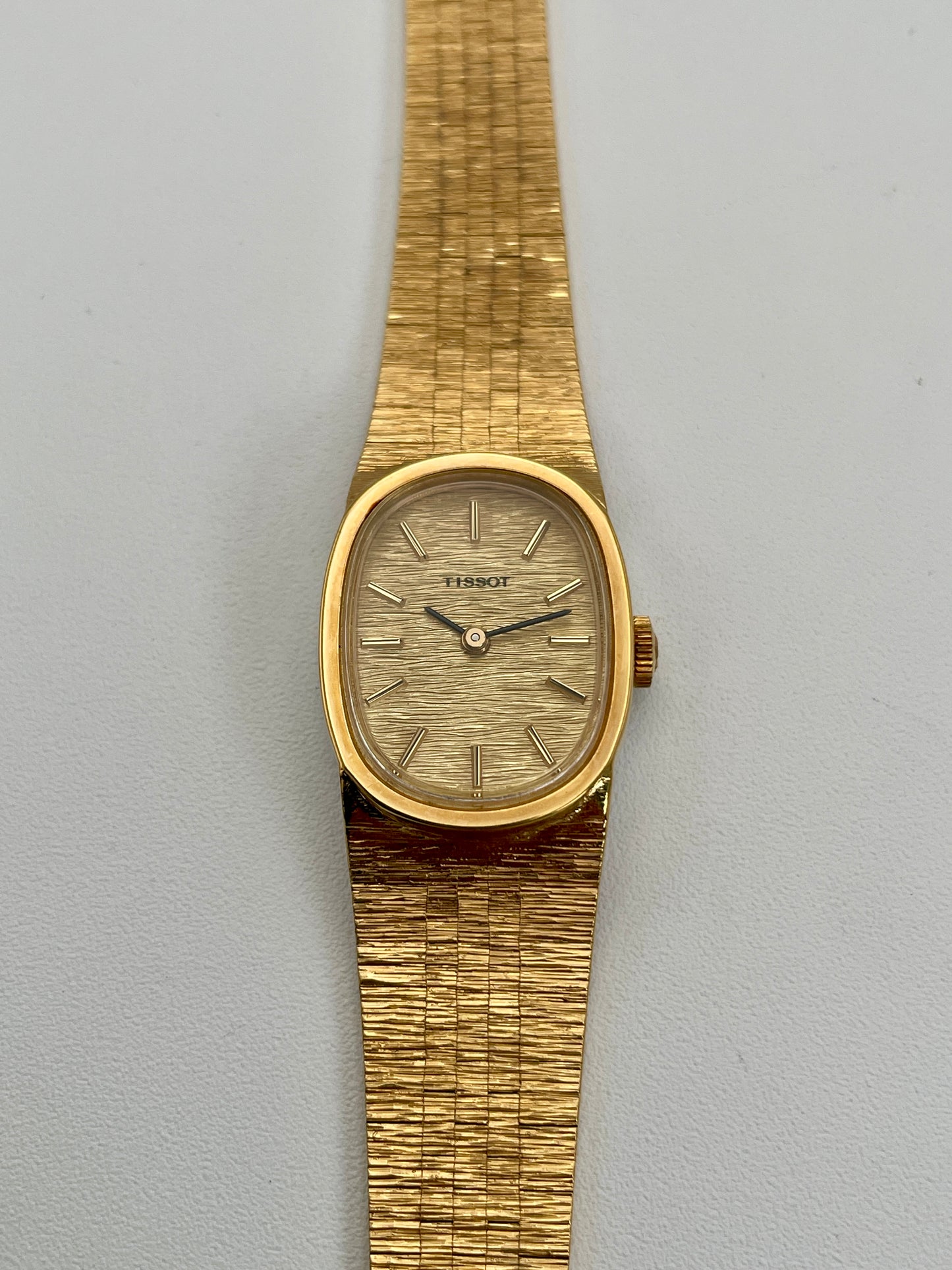 Front view of a Tissot Stylist gold dress watch showcasing the gold-tone dial, gold case, and integrated textured bracelet