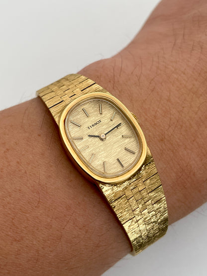 Wrist shot of a Tissot Stylist gold dress watch showcasing the elegant oval case design and integrated textured gold-tone bracelet on the wrist