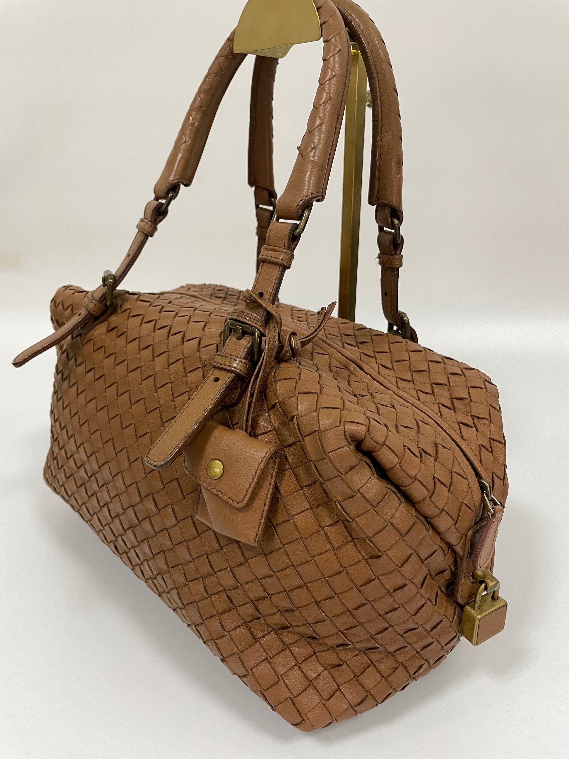 Angled view of a Bottega Veneta Intrecciato Montaigne bag in brown leather featuring a the clochette holder and a brass lock detail.