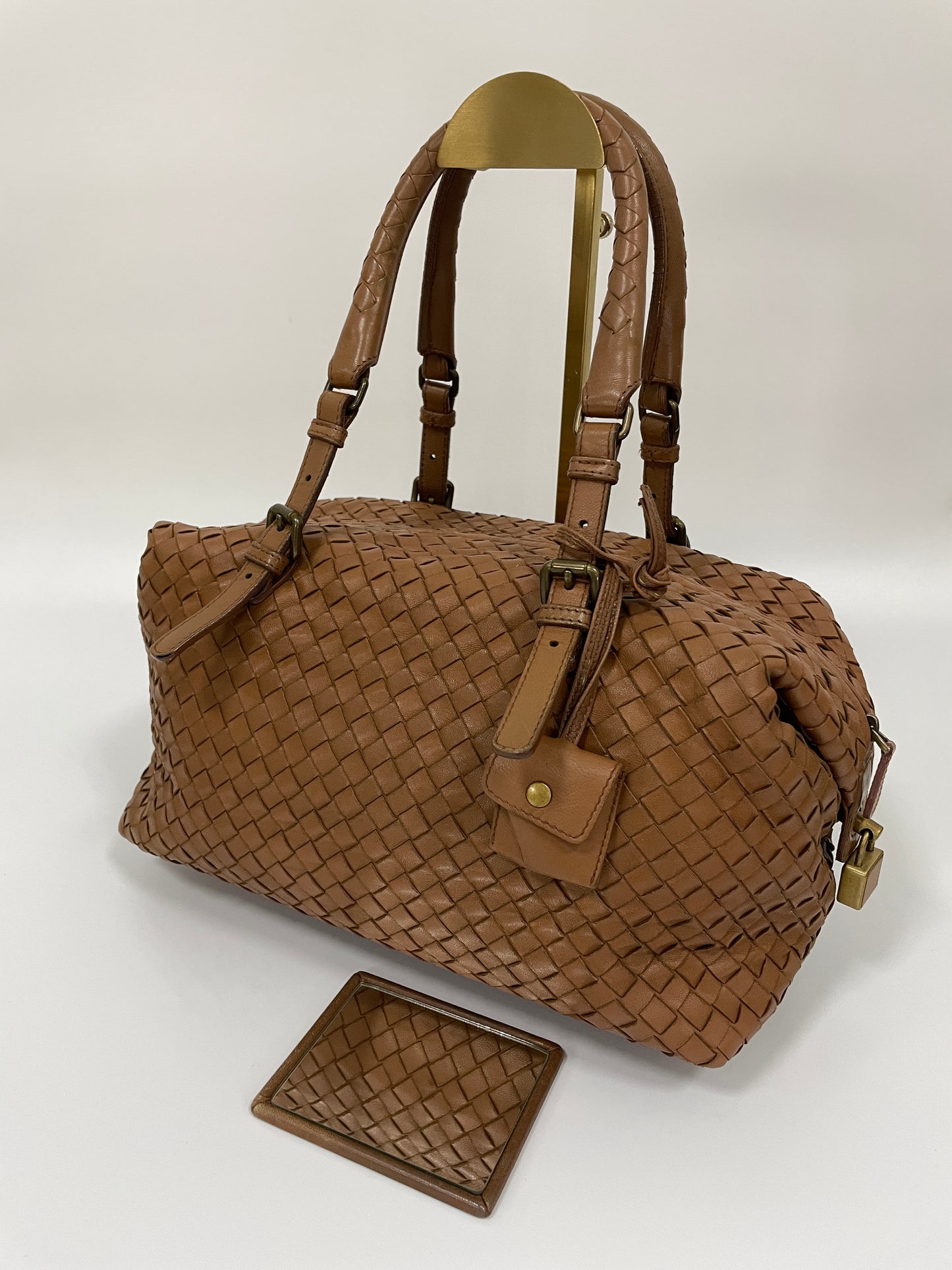 Angled view of a Bottega Veneta Intrecciato Montaigne bag in brown woven leather with dual handles and brass hardware and original Bottega mirror.