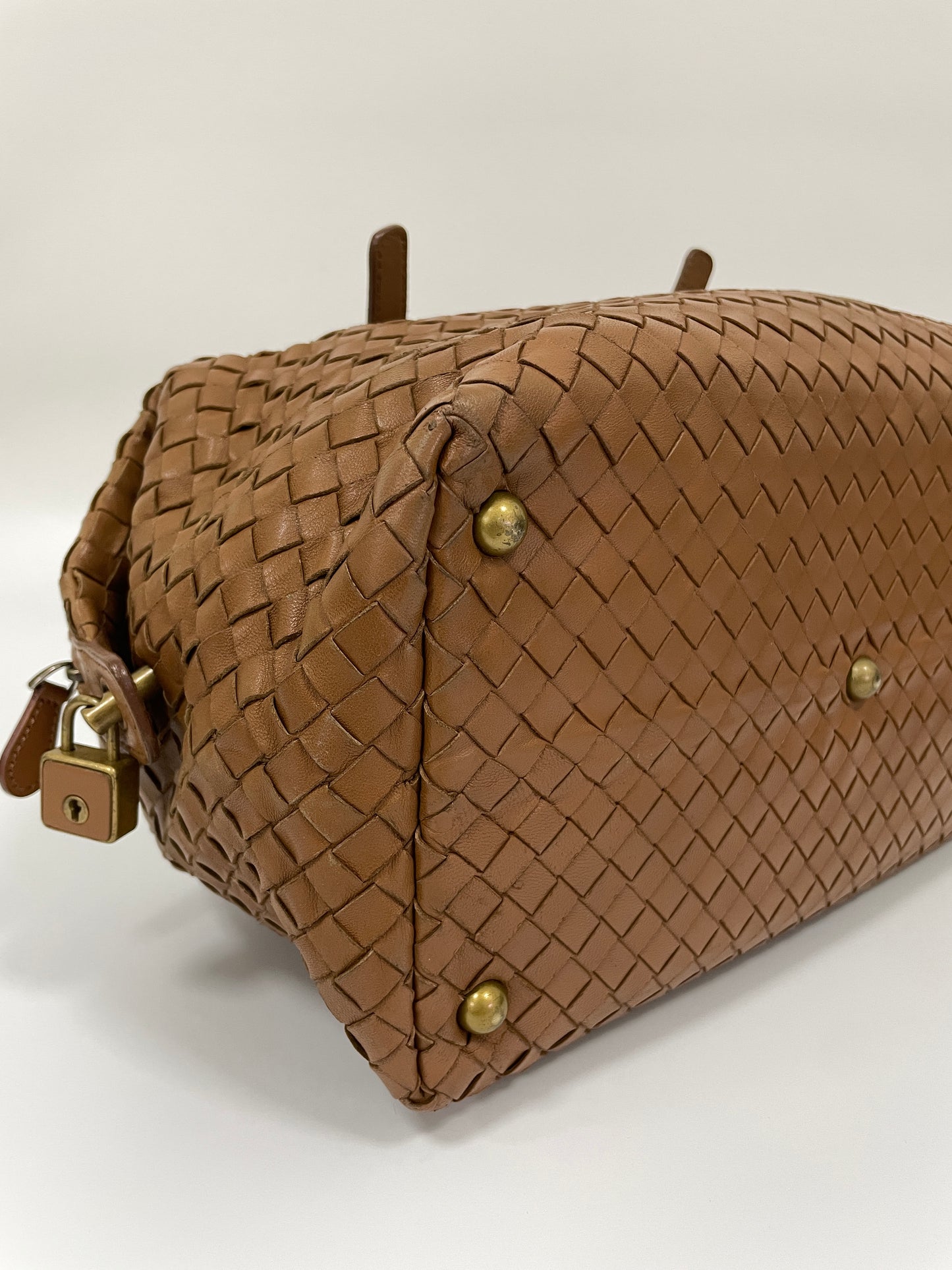 Close up view of a Bottega Veneta Intrecciato Montaigne bag in brown leather showing the woven pattern and brass feet for protection.